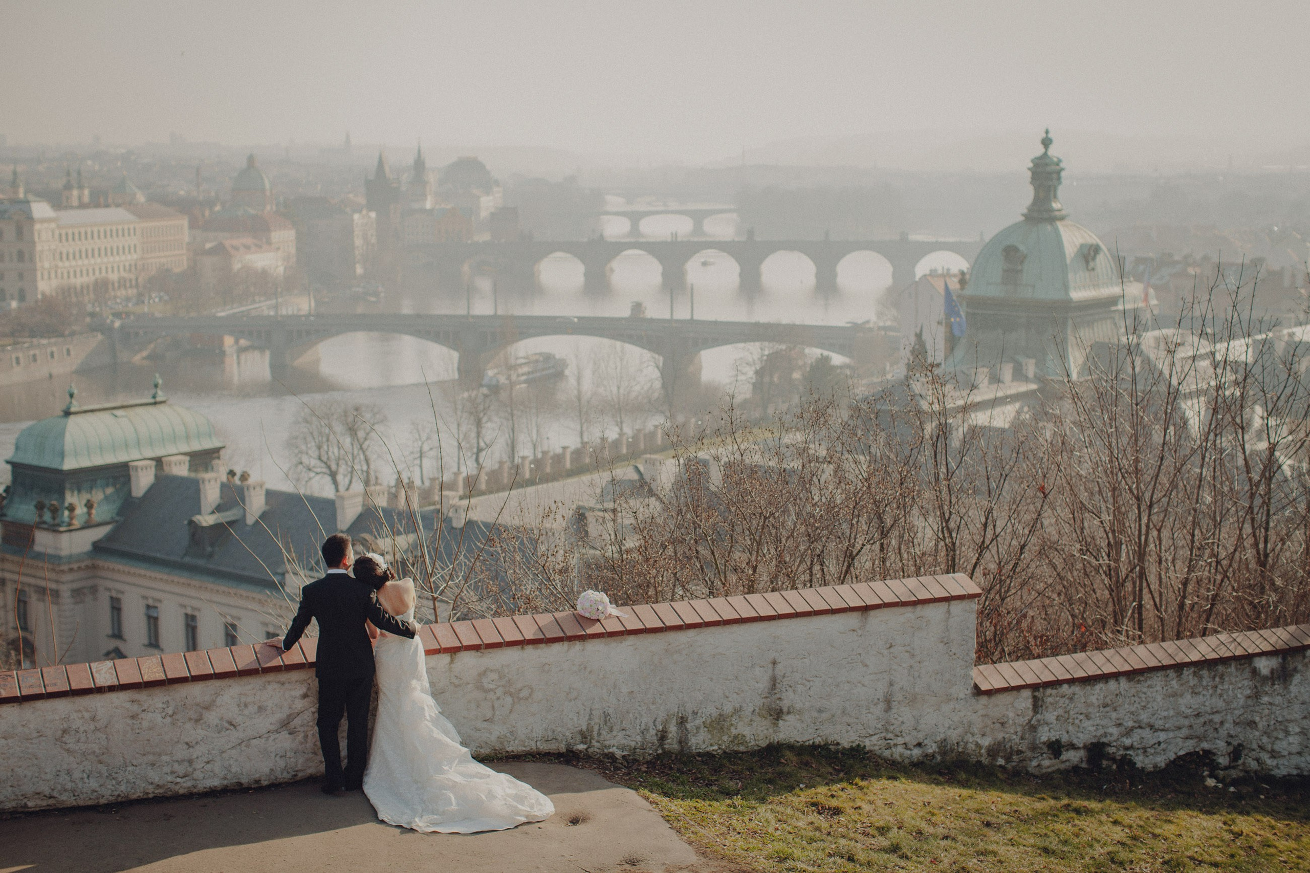 As the fog and winter mists shrouds the city of Prague below them, a Hong Kong bride & groom snuggle up as they enjoy the view.