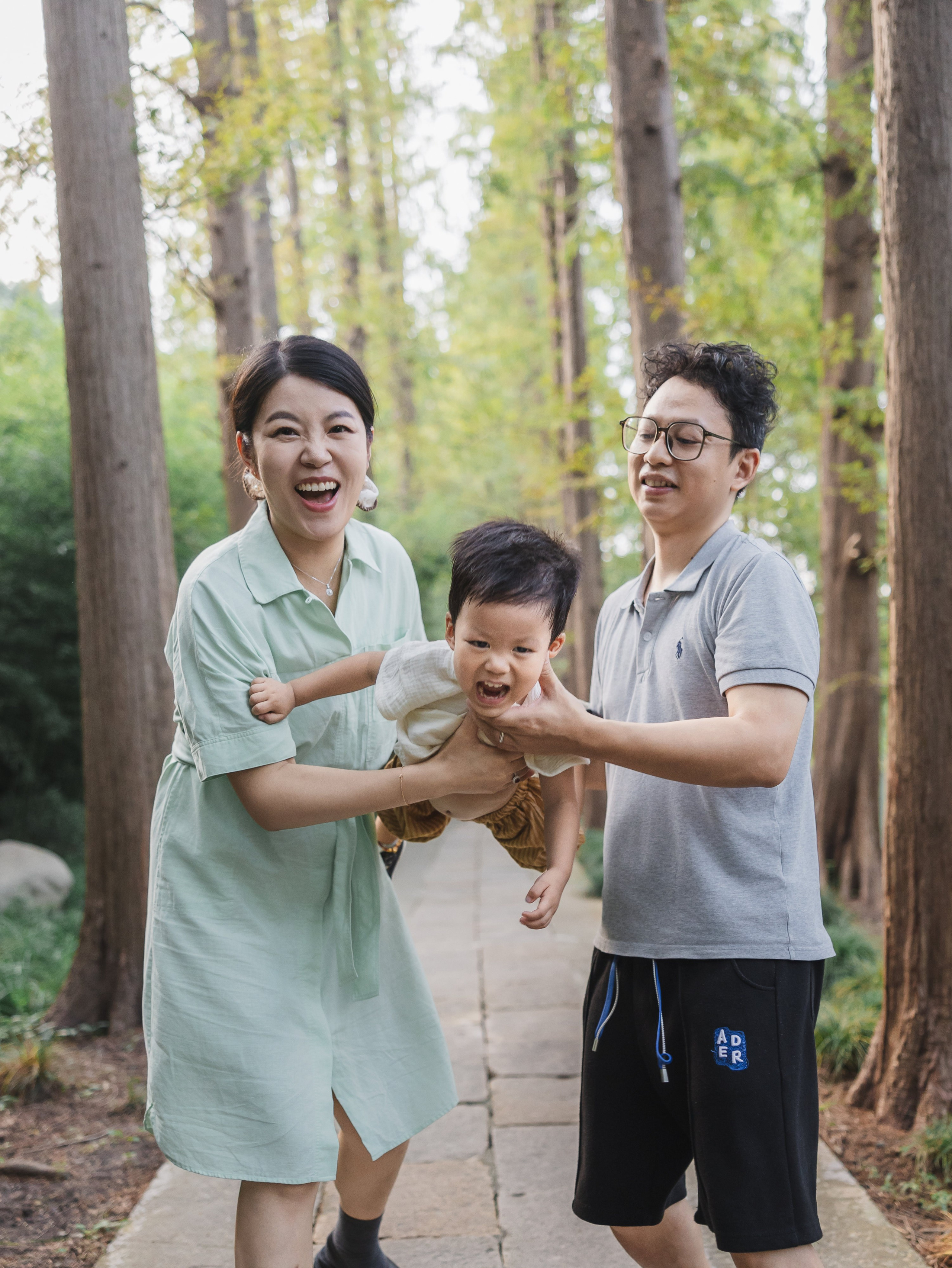 Parents smile at their toddler in a forest path, creating a warm documentary family portrait.
