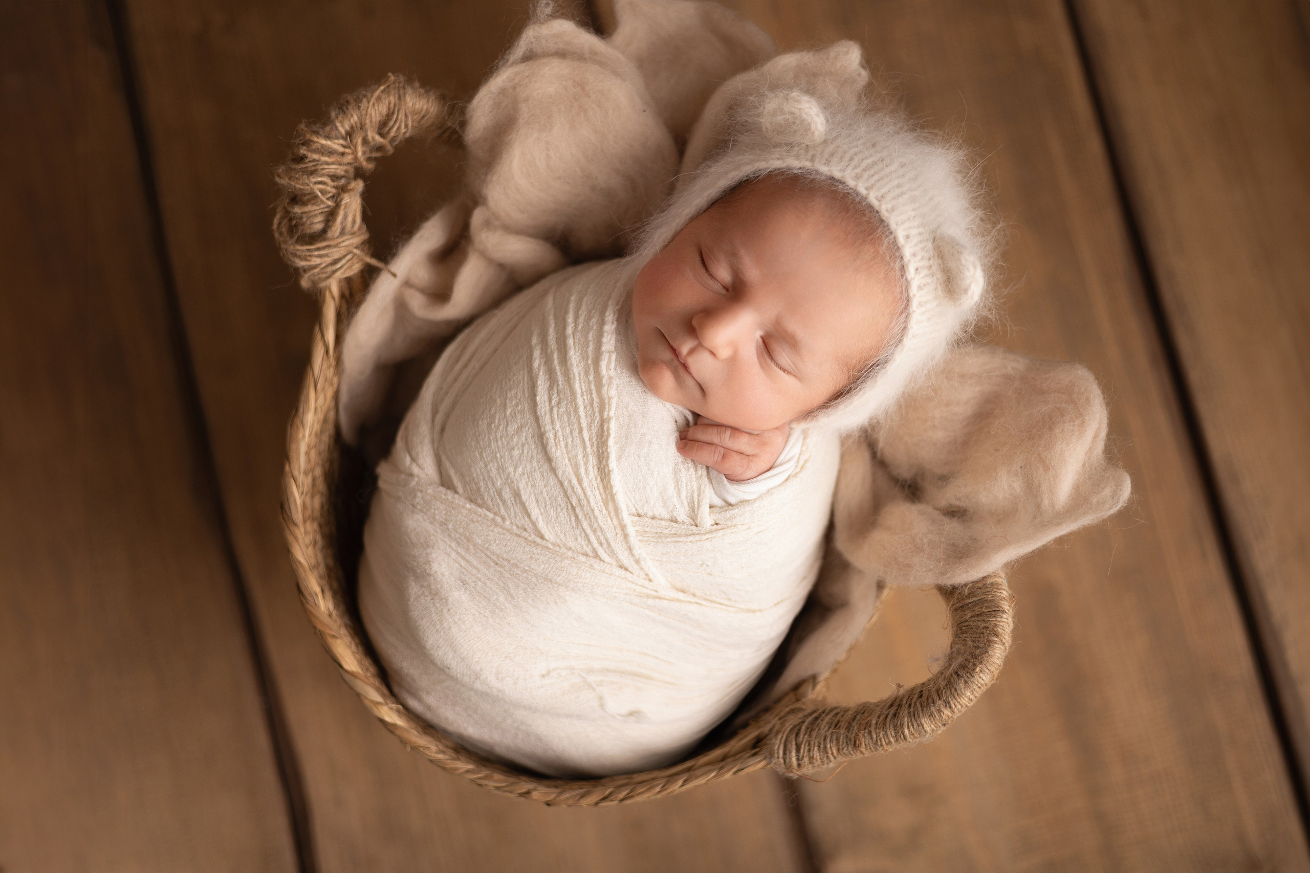 Frisch geborenes Baby eingewickelt in eine Decke, liegt in einem rustikalen Körbchen – Newbornfotografie in Iserlohn