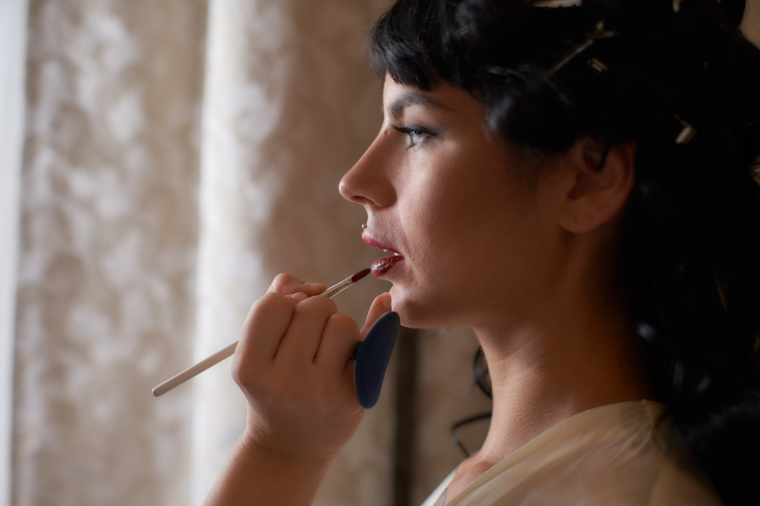 Makeup artist applying lip gloss to tattooed bride Courtney during intimate prep.