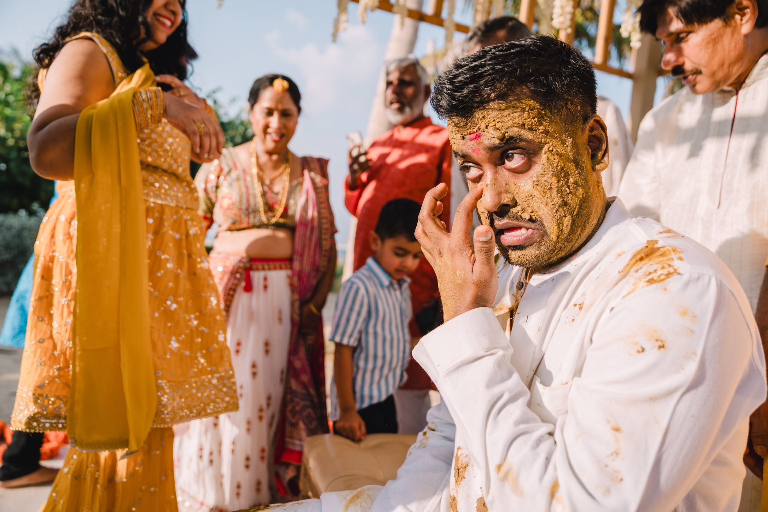 the indian gentleman on a turmeric ceremony is trying to clean his eye in a cute way