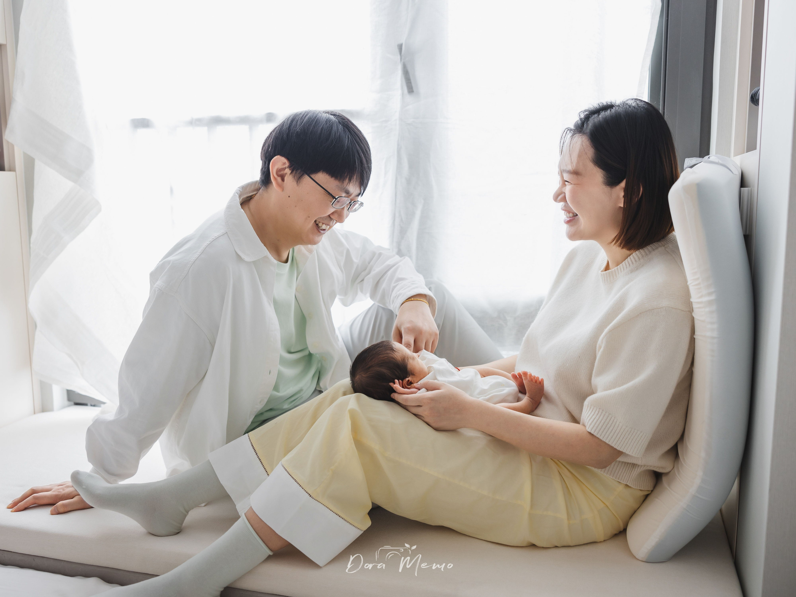 Father gently touching his newborn grandchild's hand while the mother watches, three generations together