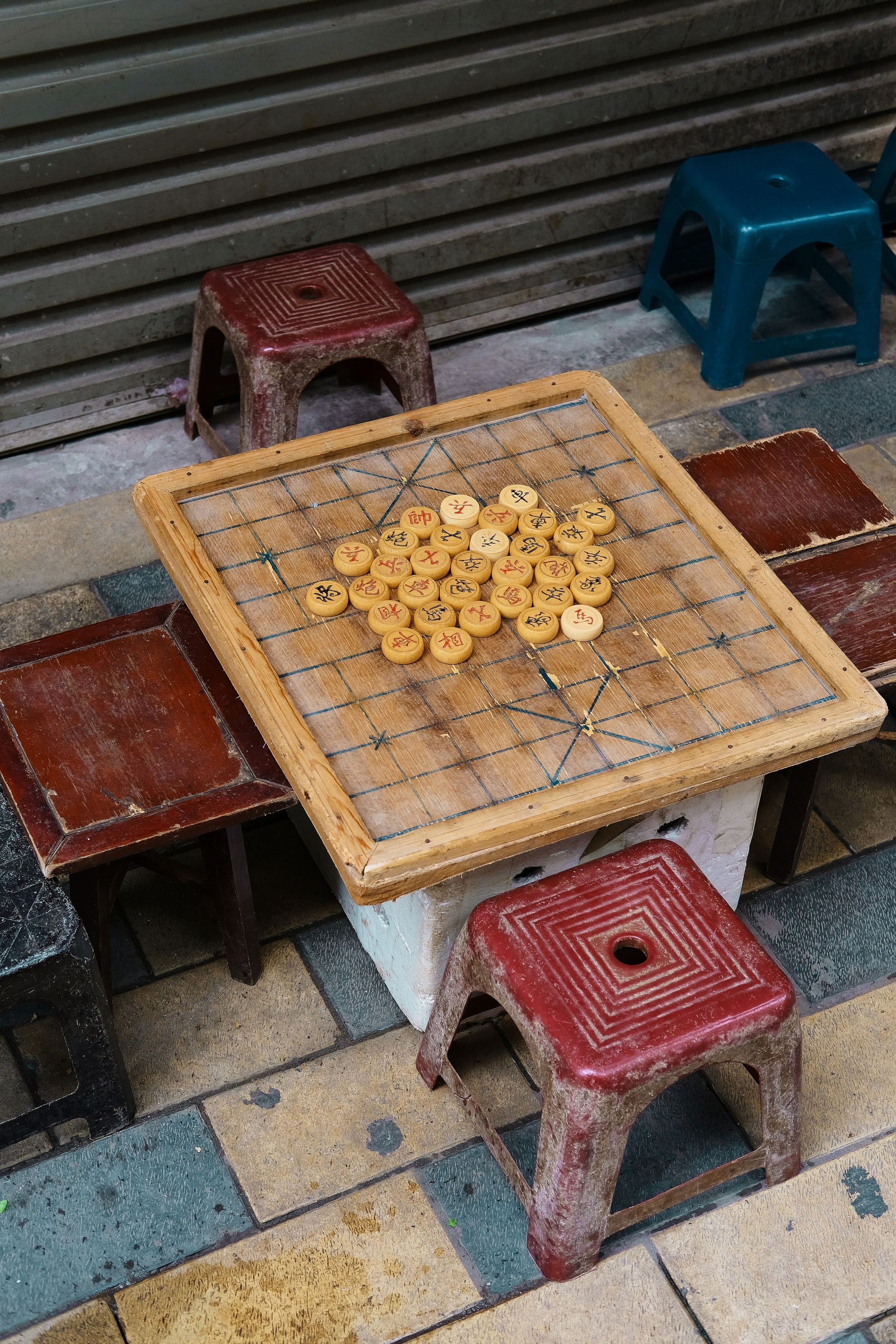 It’s a traditional Chinese strategy board game, often played outdoors on small tables like this. The round pieces with Chinese characters and the grid with diagonal lines in the center are classic Xiangqi features.