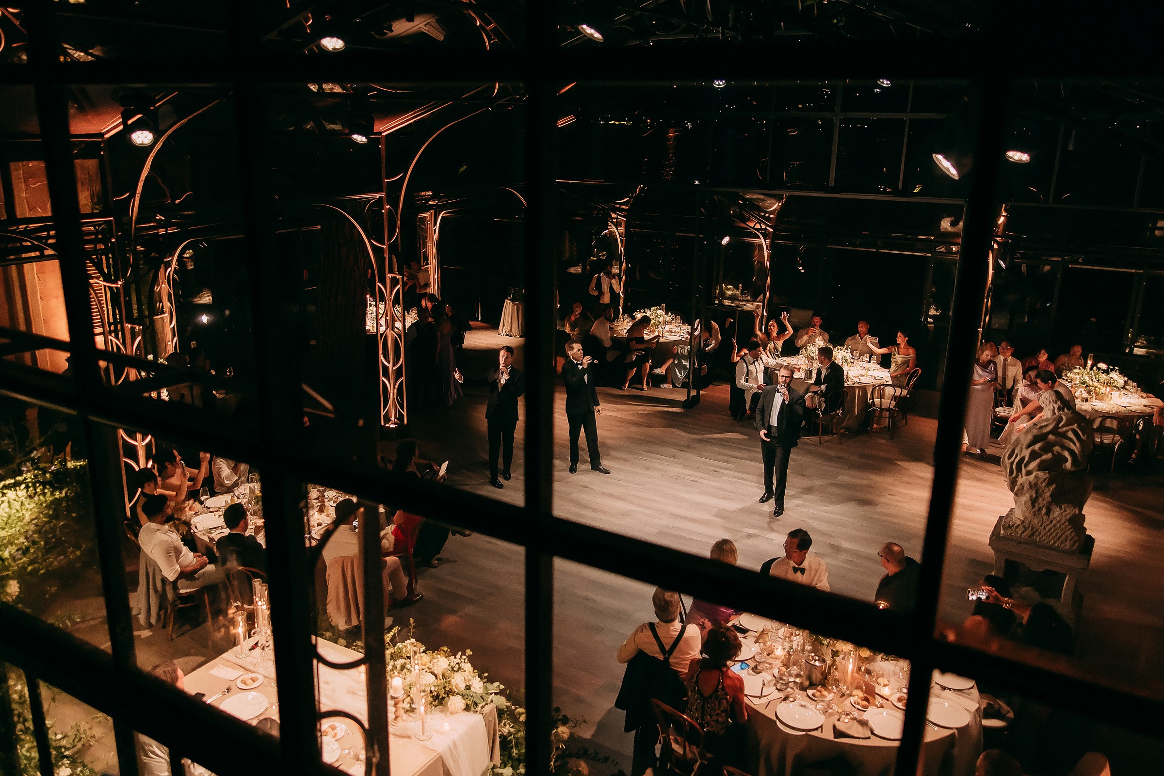 Overview of wedding reception through glass windows, showcasing lively ambiance.