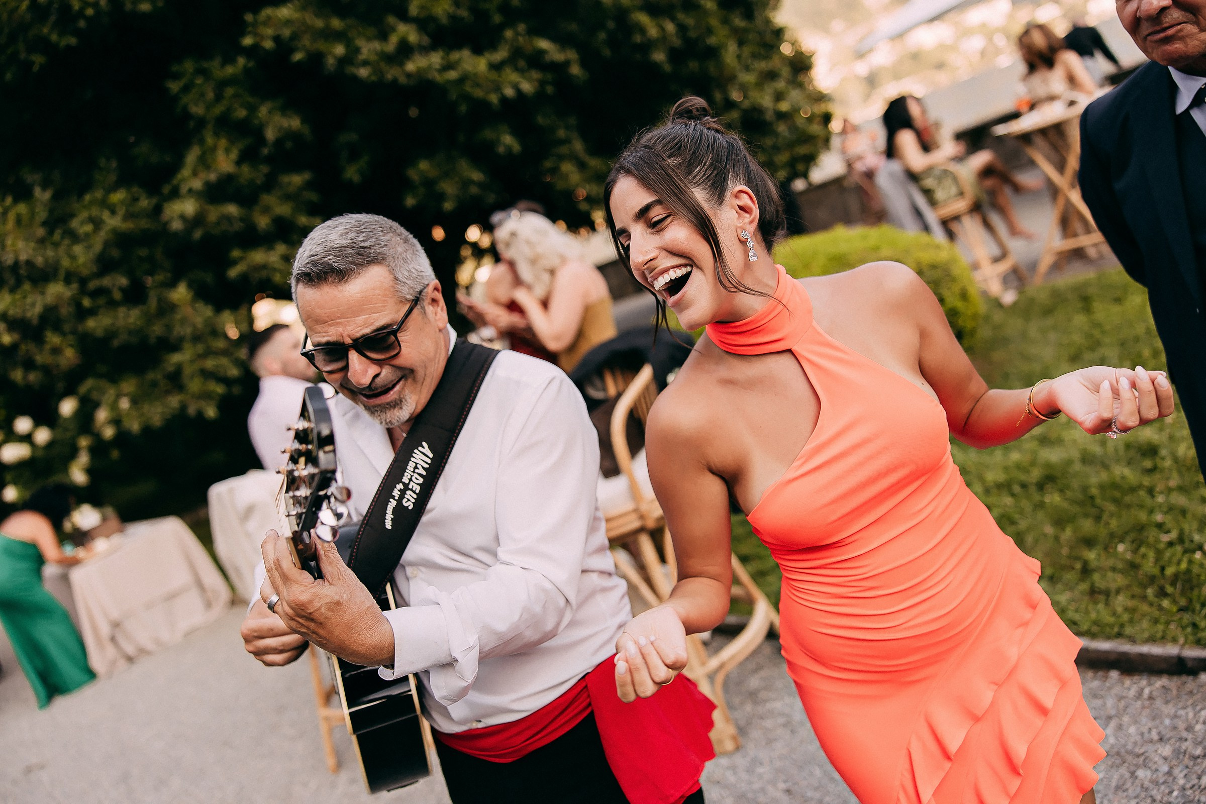 Woman in orange dress joyfully dances alongside the guitarist at the celebration.