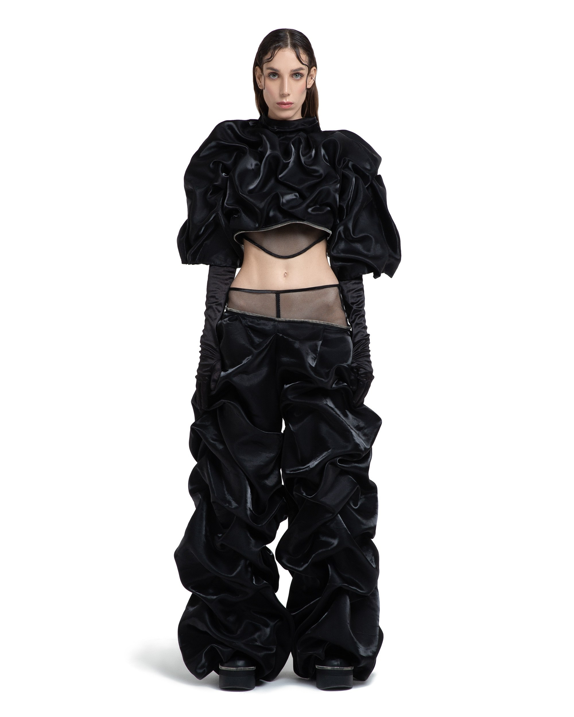 Woman in a high-fashion black outfit with voluminous ruffles, posing on a plain white backdrop