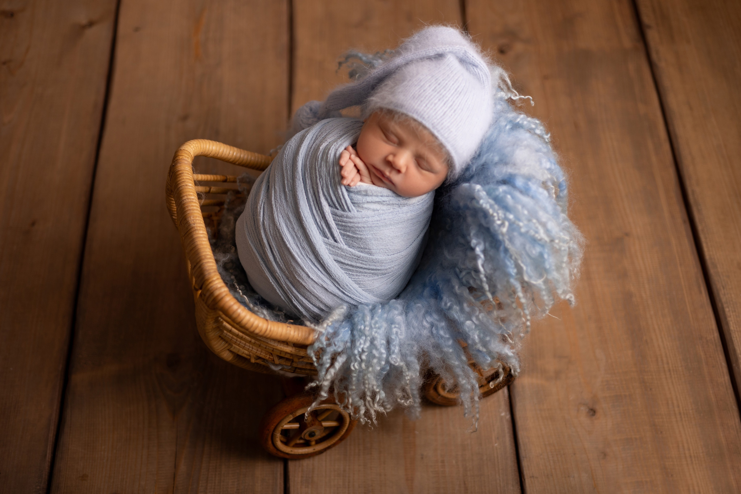 Frisch geborenes Baby eingewickelt in eine Decke, liegt in einem rustikalen Körbchen – Newbornfotografie in Iserlohn