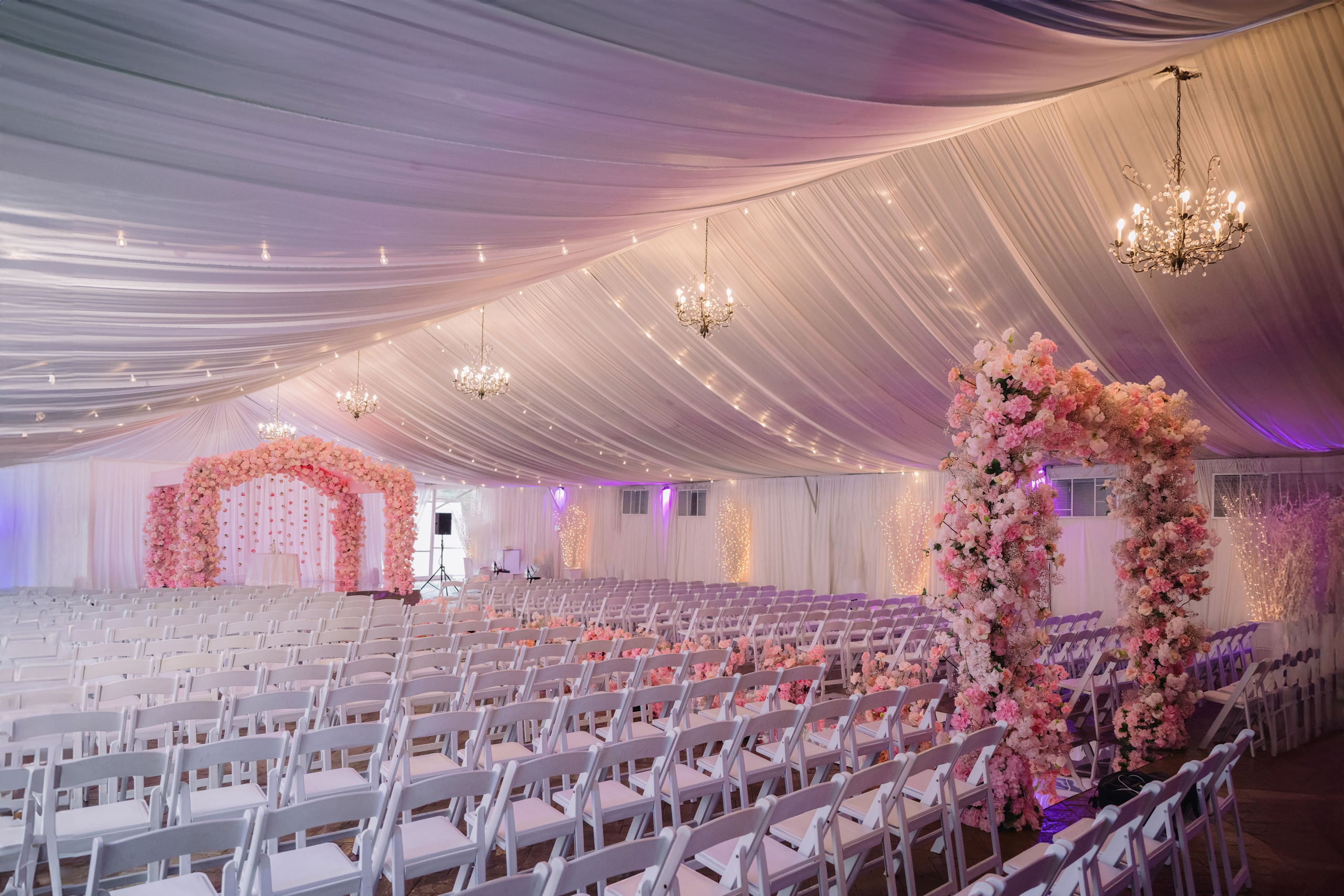 a wedding tent with white chairs and pink flowers