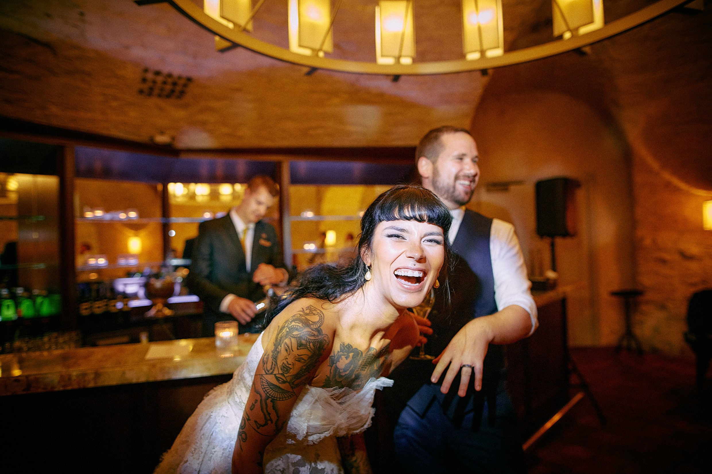 Tattooed bride bursting with laughter beside smiling groom