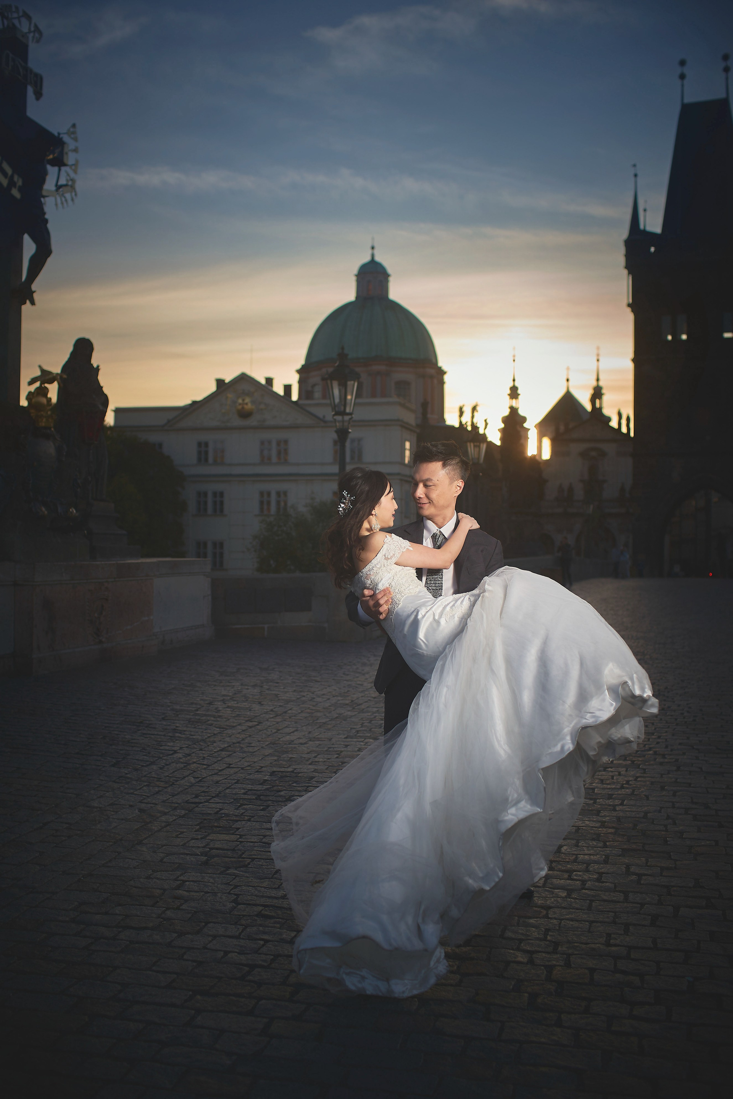 Groom Conan spinning bride Eva near the Cavalry statue at sunrise on Charles Bridge.