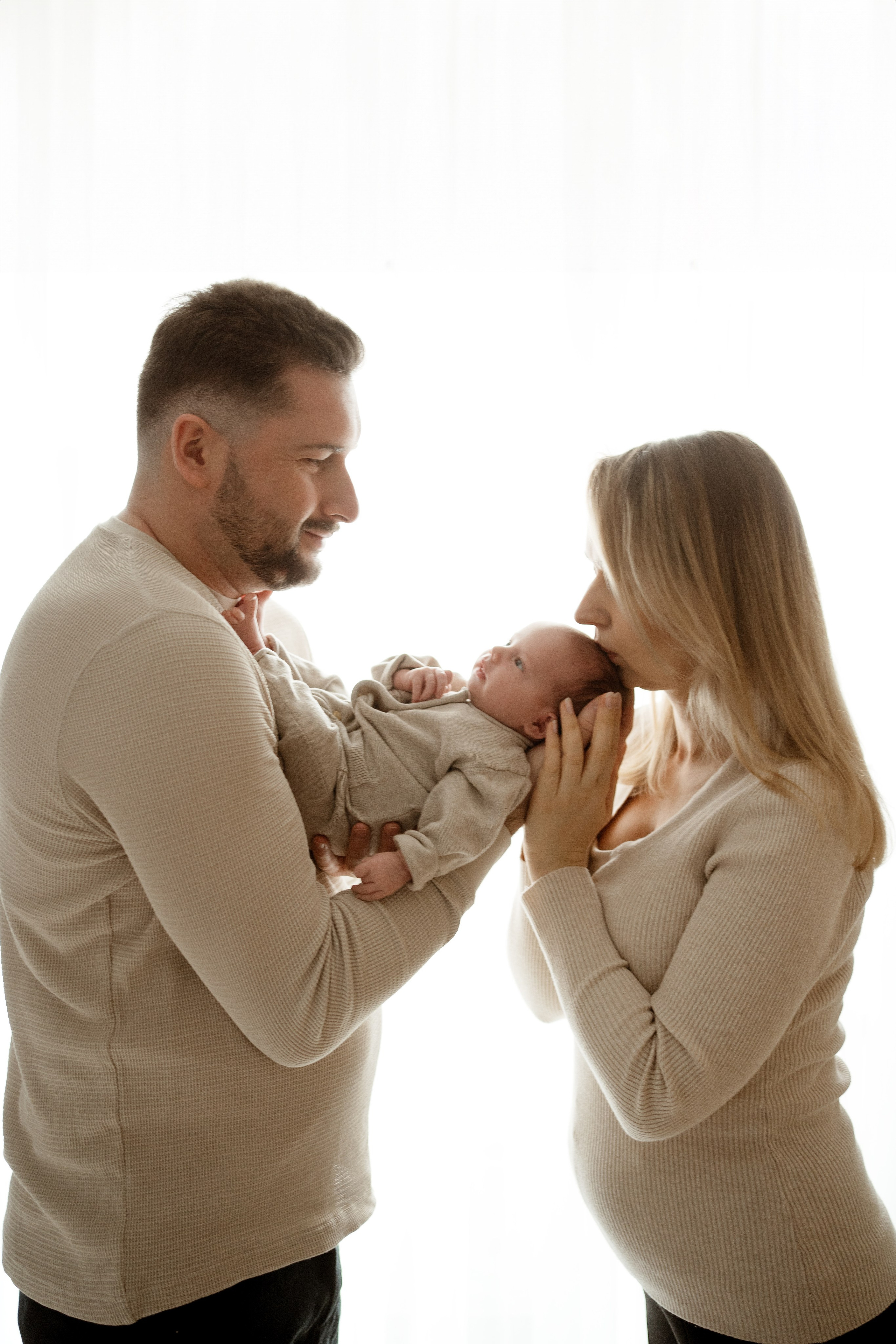 Noworodek w ramionach rodziców na tle okna – fotograf Łódź