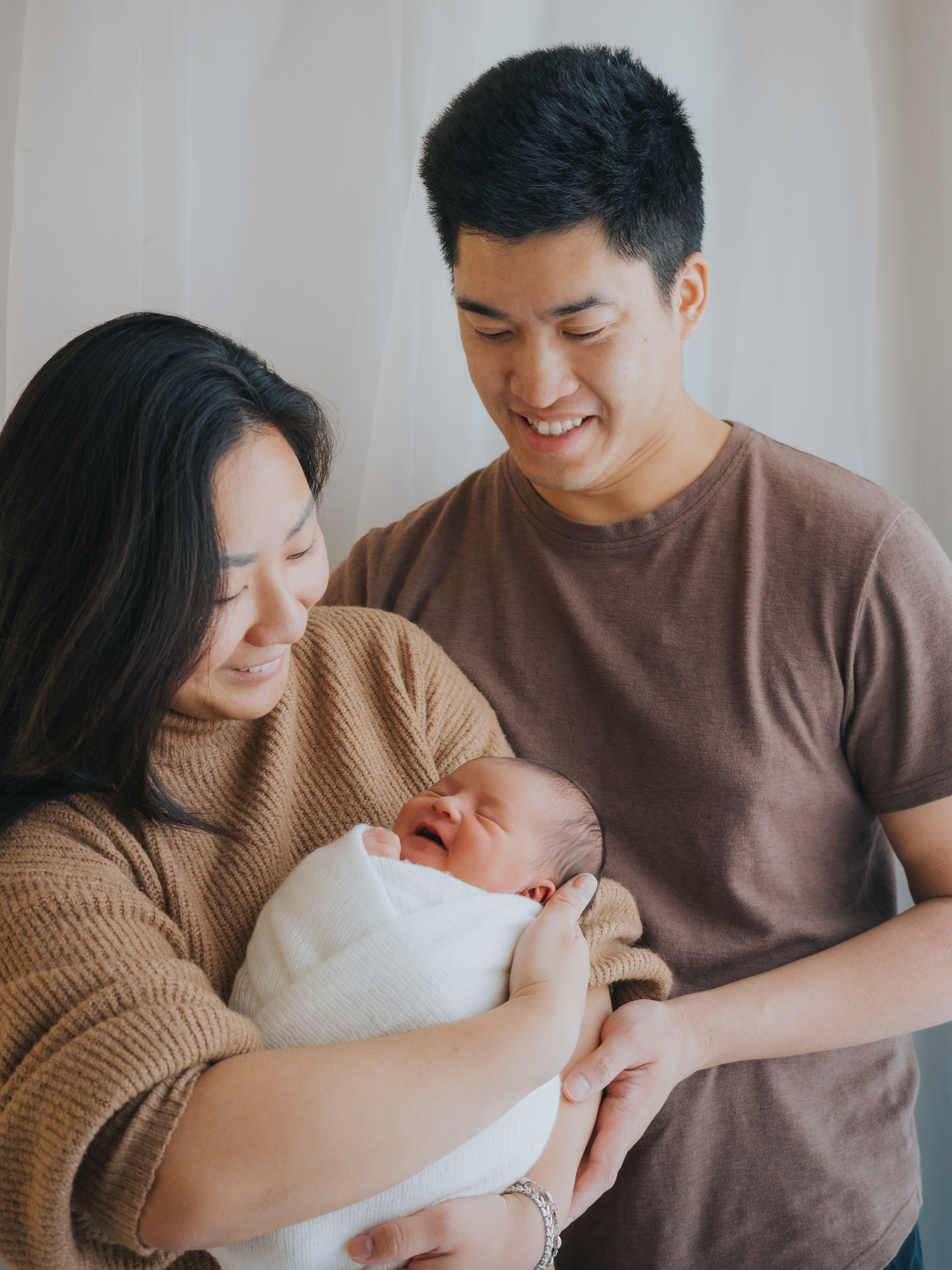 Family photo of a young family, mother and father holding newborn baby.