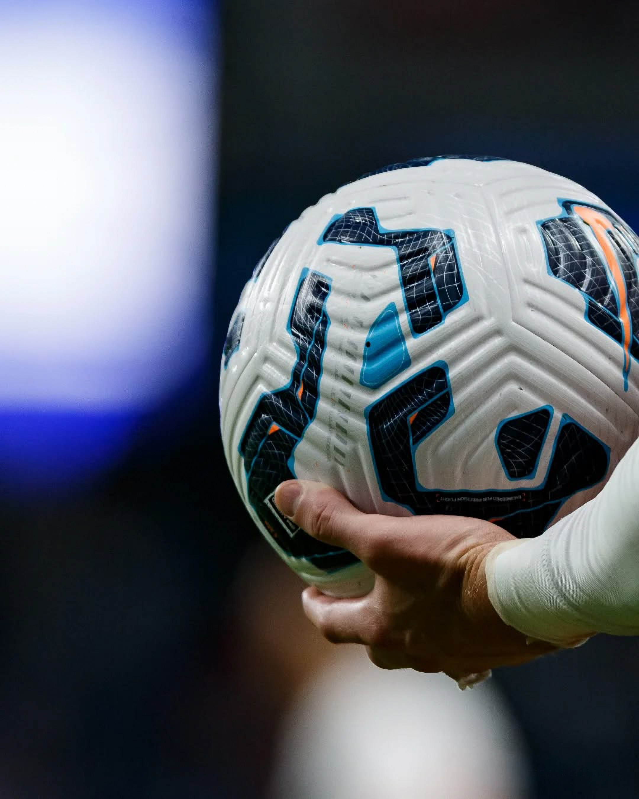 Close-up of a football held by a player during a match, professional football photography with shallow depth of field.