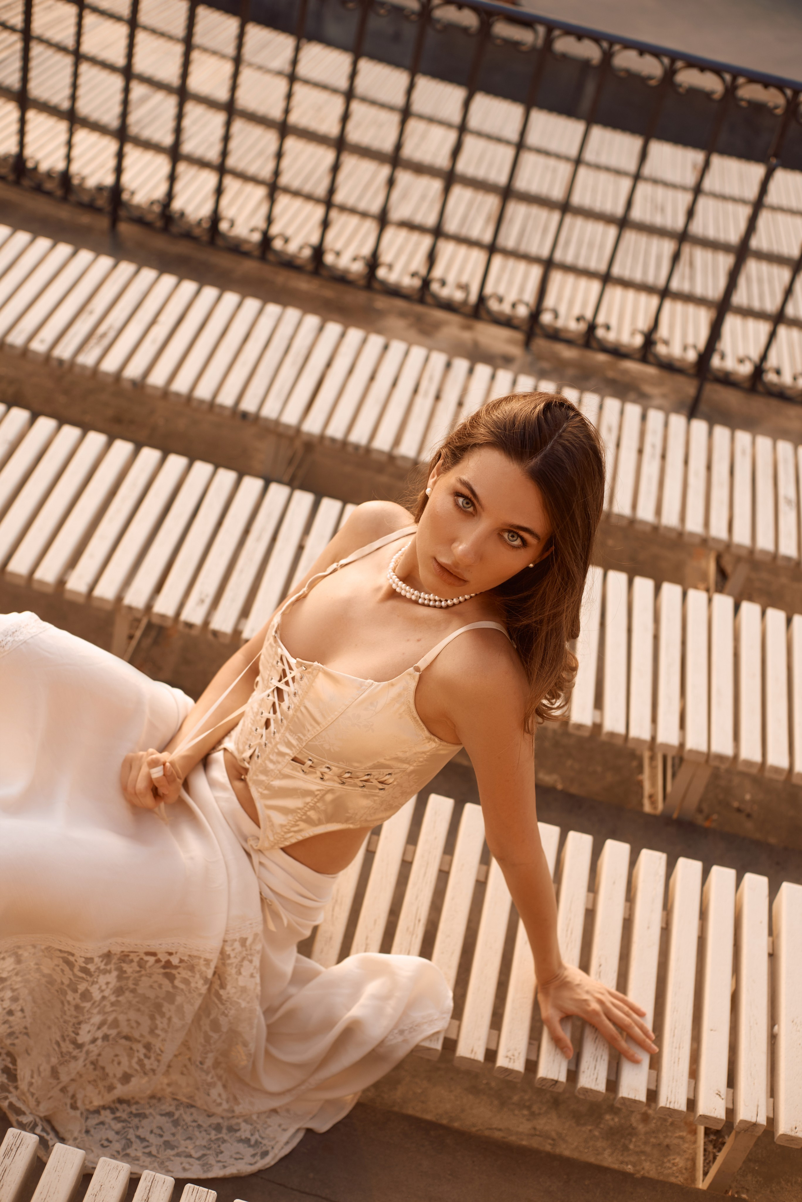 Золотий відблиск заходу – Дівчина в ніжному образі сидить на сходах, освітлених останніми променями сонця. Її погляд глибокий і загадковий.