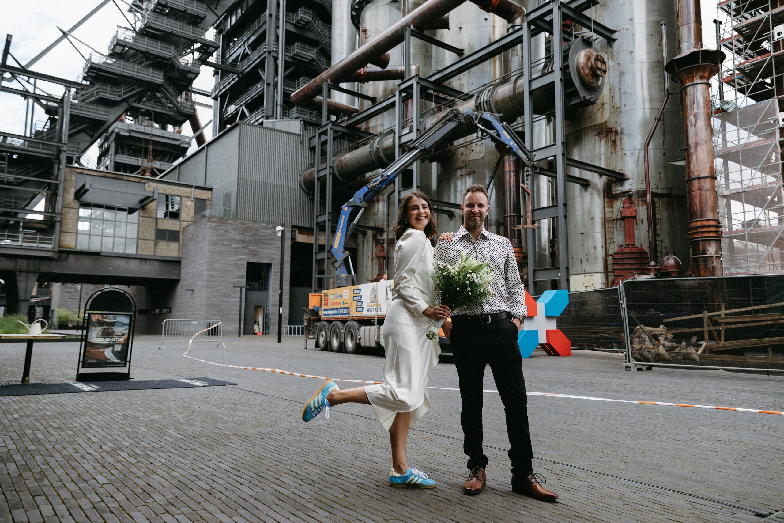 Verspieltes Hochzeitspaar posiert vor industrieller Kulisse in Belval