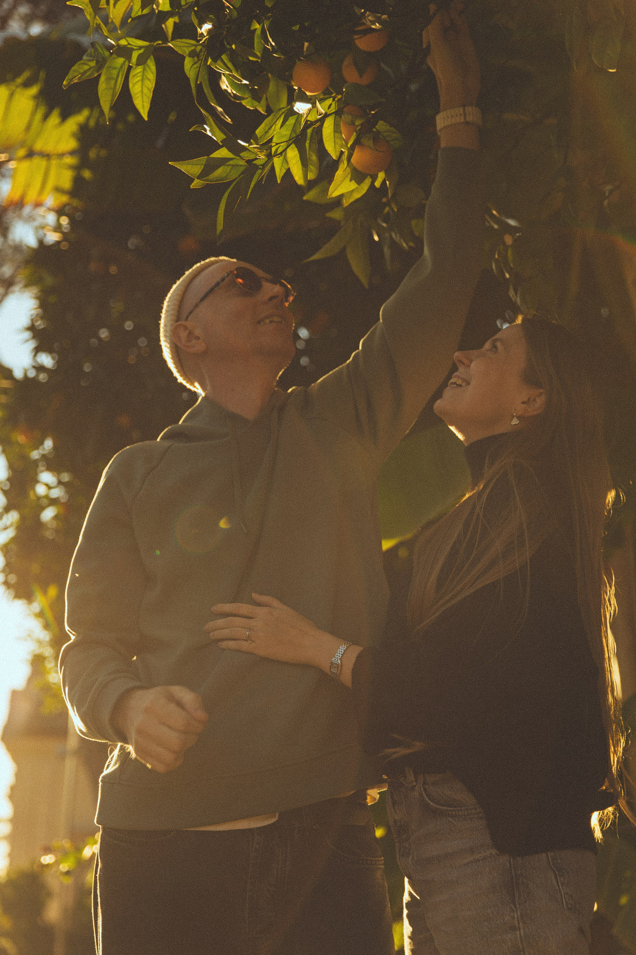 A candid photograph of a couple collecting oranges in the park in Rome, their expressions full of joy.