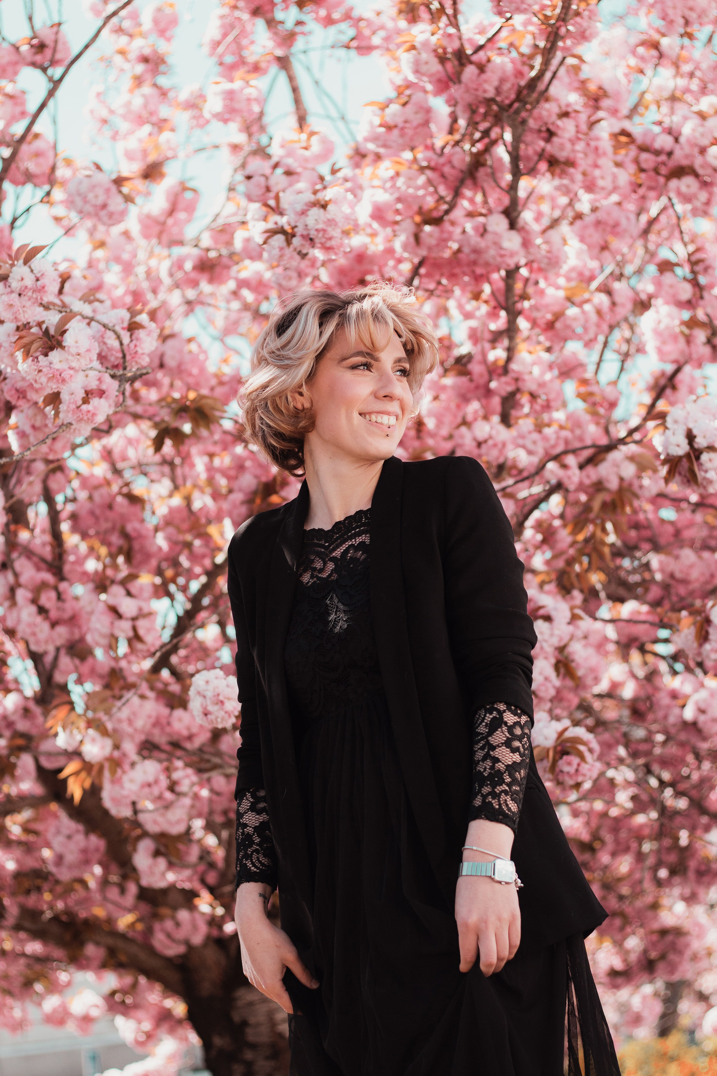 Une femme blonde, habillée en noir, à côté d'un arbre fleuri