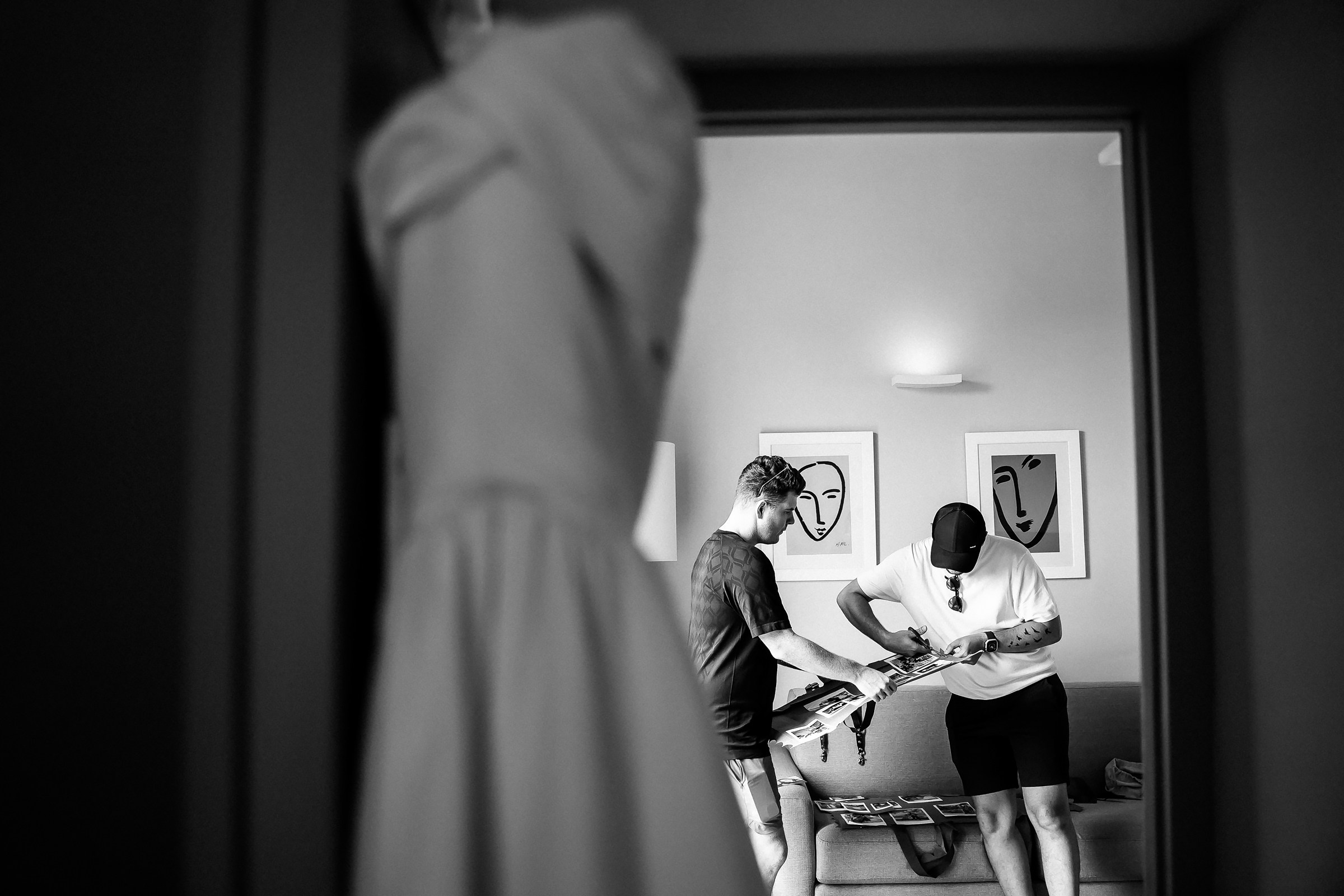 A candid black-and-white moment of two groomsmen preparing details for a wedding day.