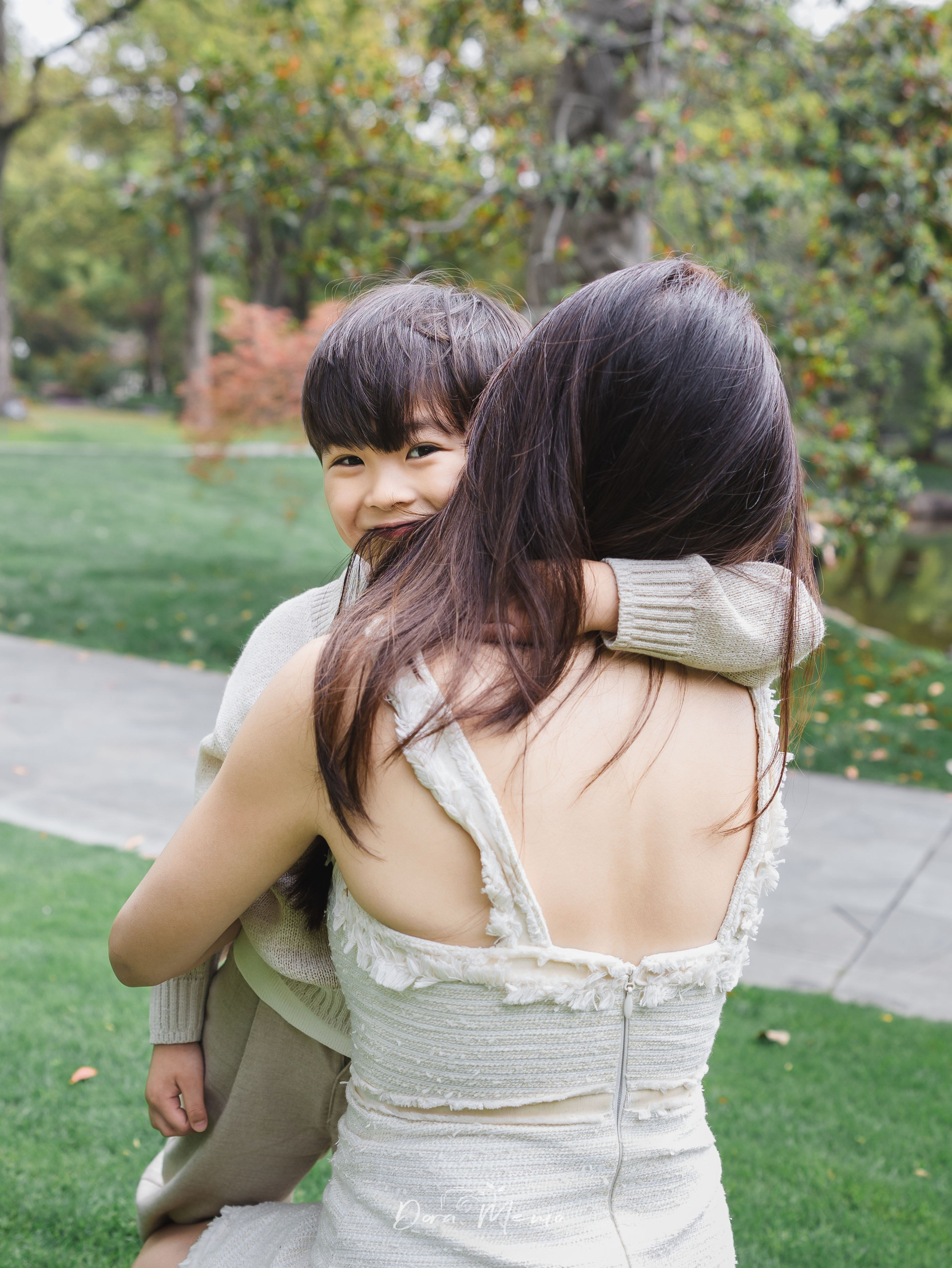 A young boy rests his head on his mother's shoulder, eyes crinkled with a smile