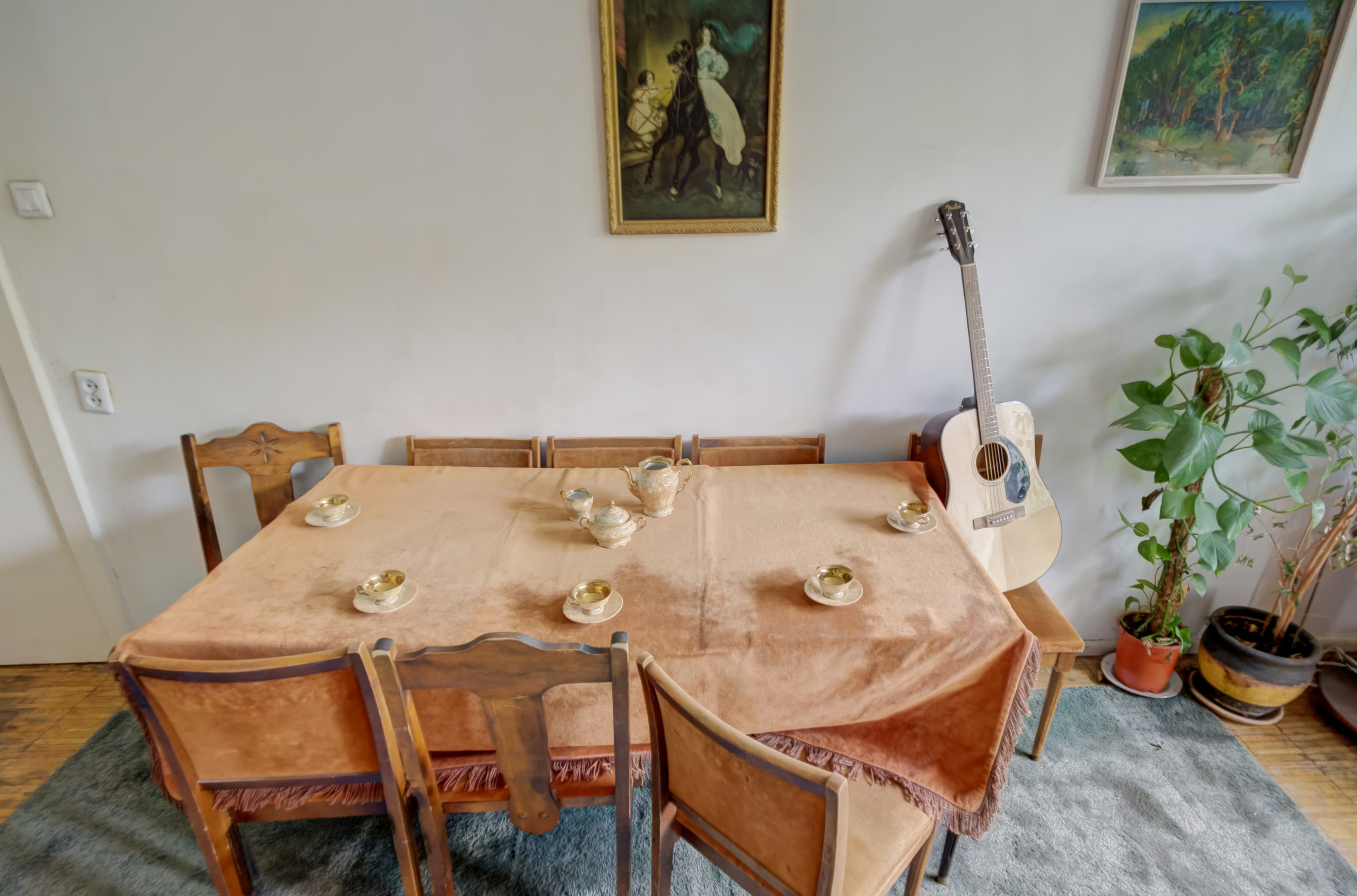 Klasikinis valgomojo stalas su servizu ir gitara, pastatyta šalia šviesios sienos.