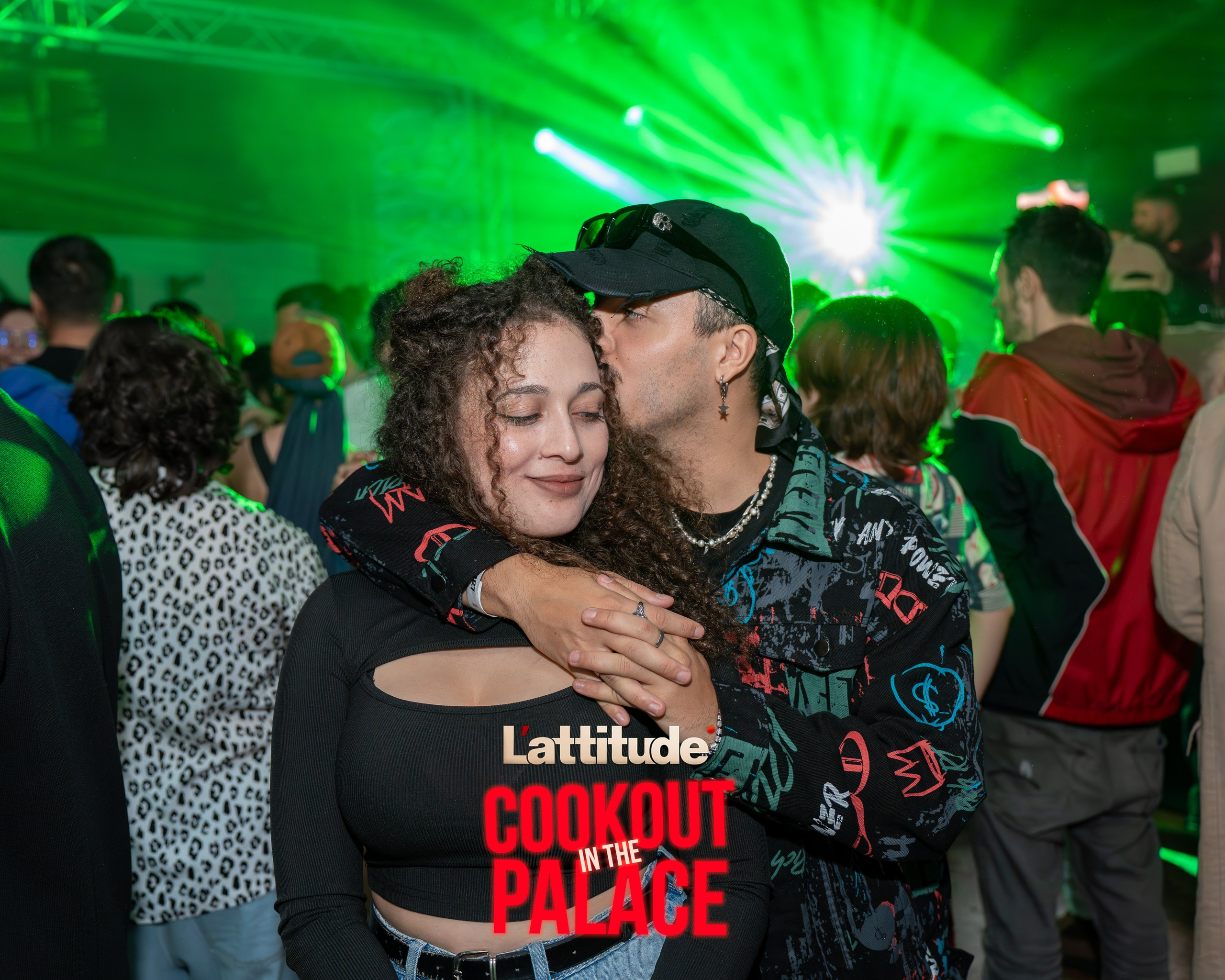 Man embracing and kissing a woman on the cheek at a crowded event with green stage lighting.