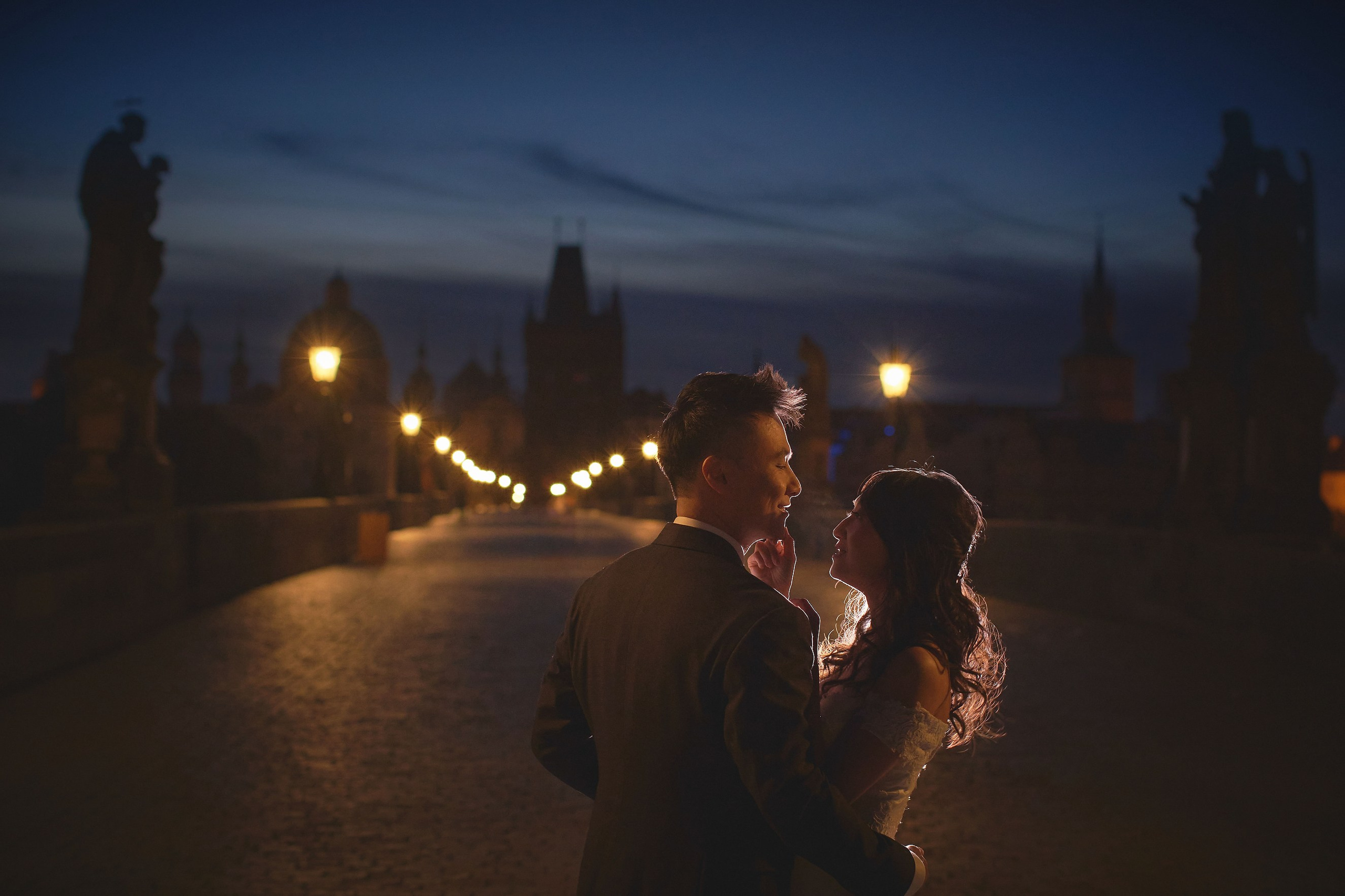 Silhouetted newlyweds Eva and Conan under gas lamps and statues on Charles Bridge at dawn.