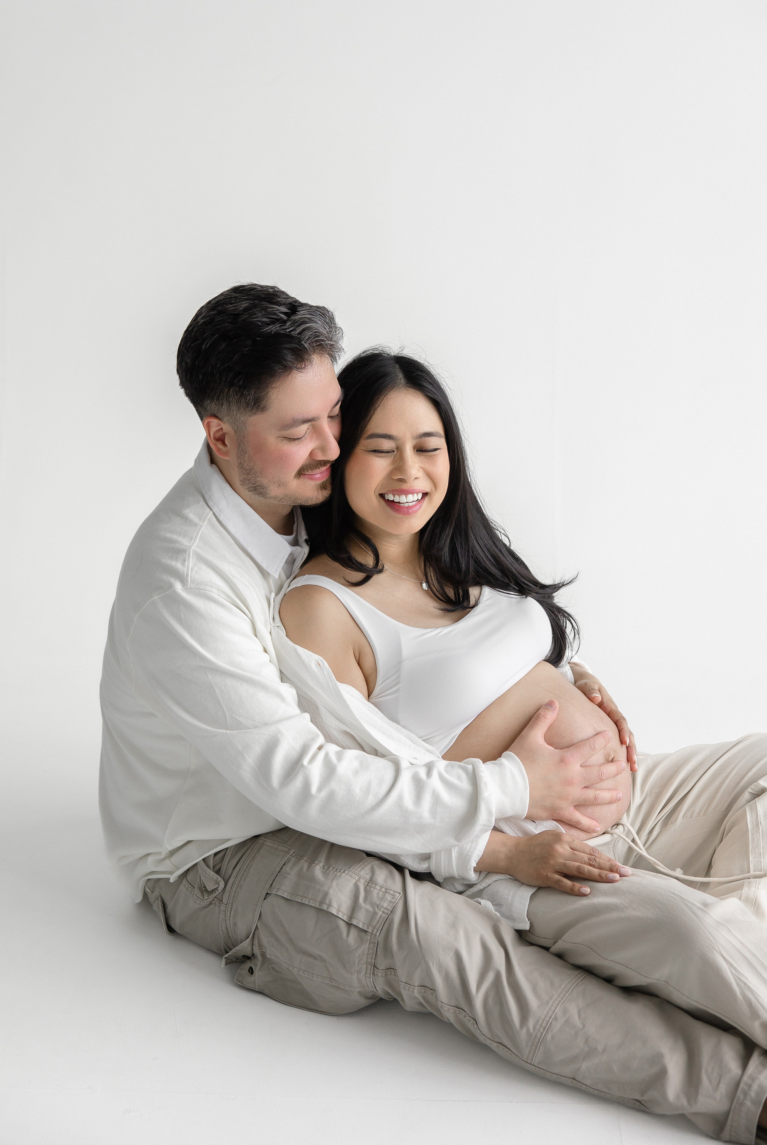 Happy couple sitting together during maternity photoshoot – natural, intimate pregnancy photography in Toronto studio by Iana Banana