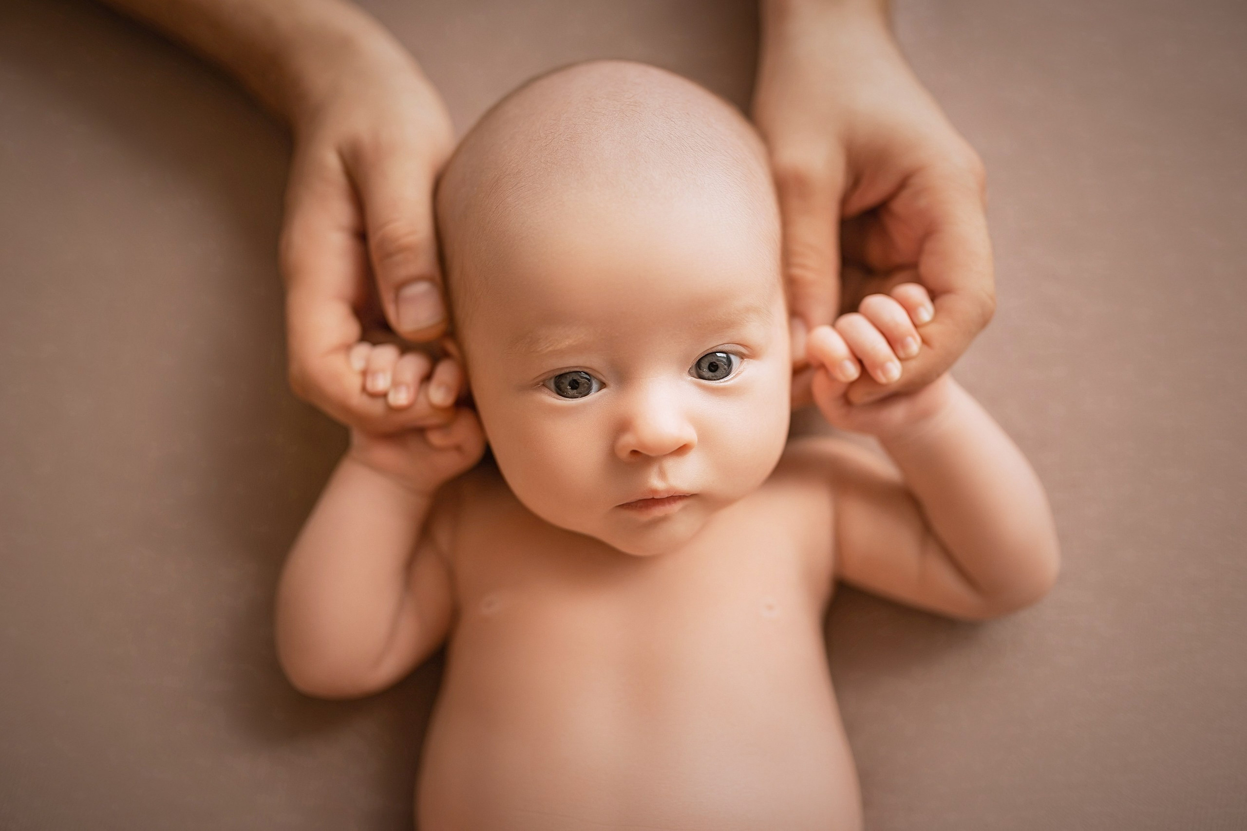 Newborn baby lying on back, gazing curiously while mother holds hands