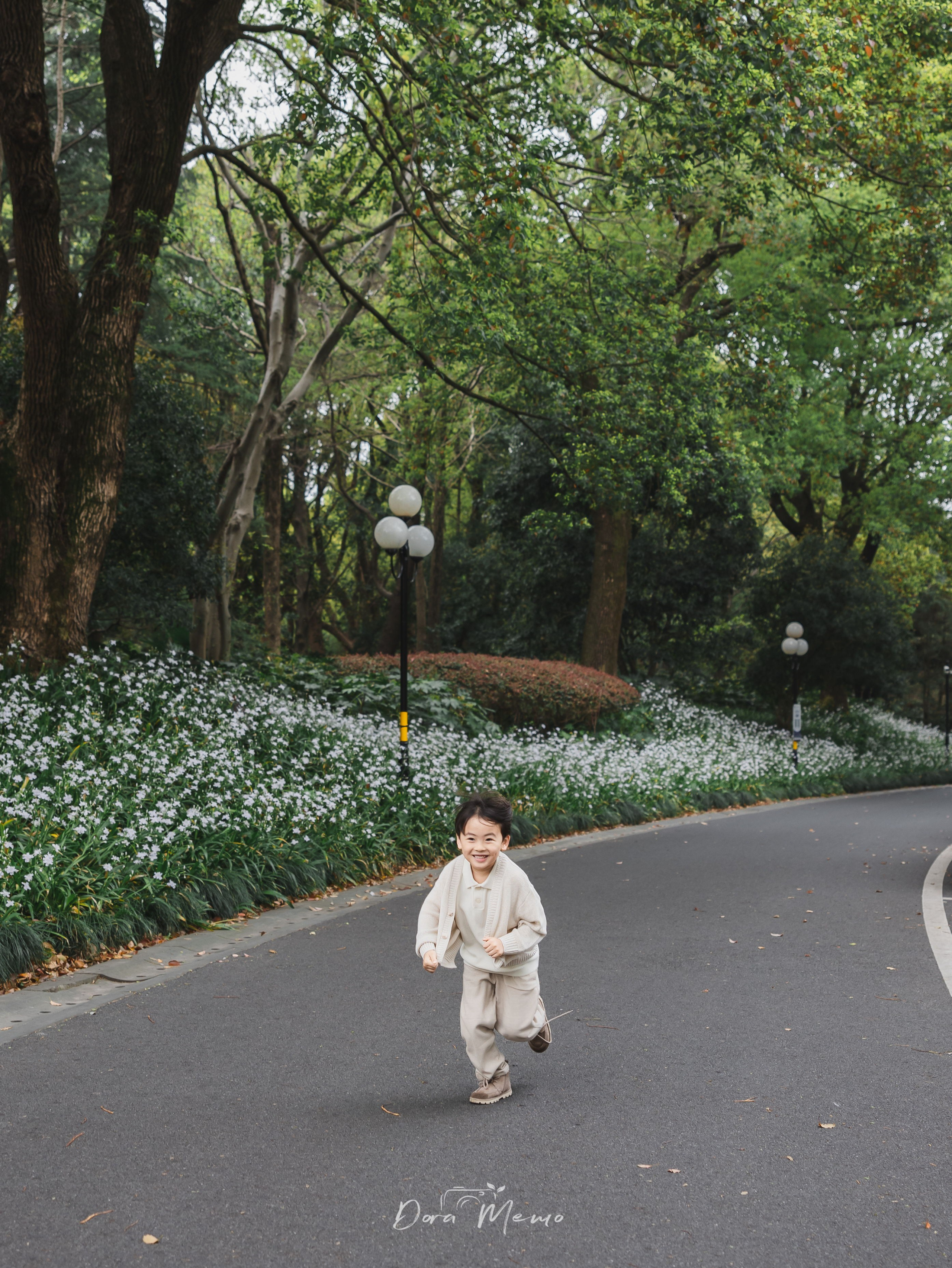 A boy runs freely along a path lined with white flowers, captured by a Shanghai family photographer