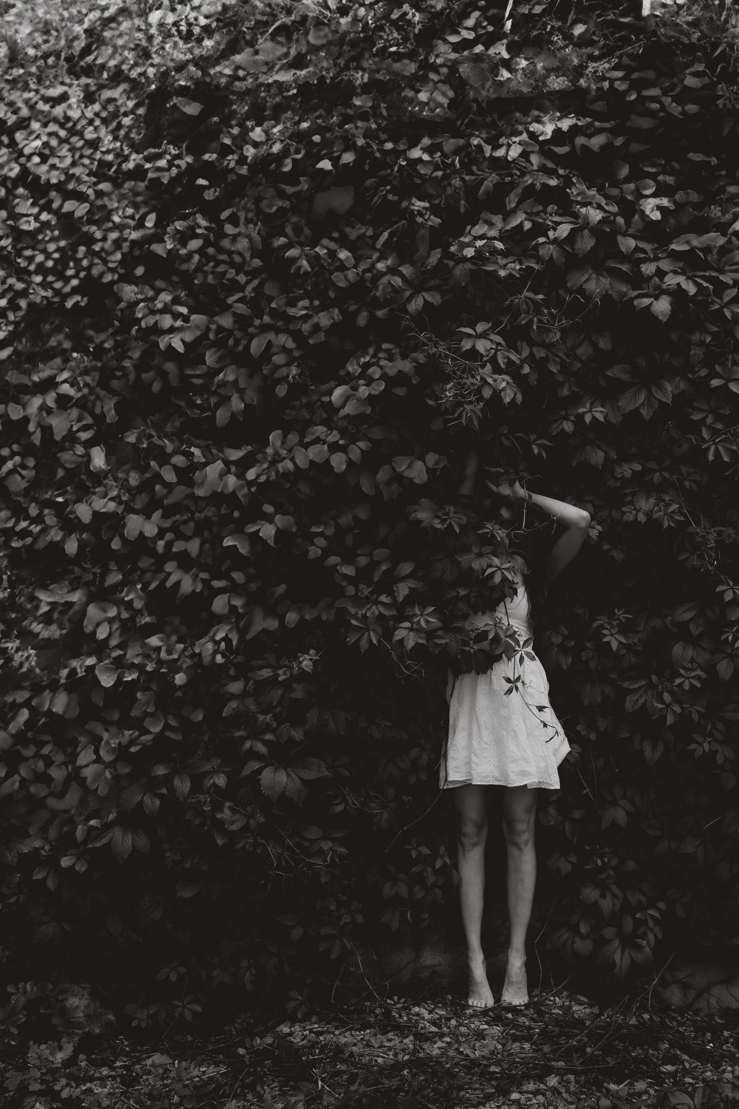 Fine art portrait of a woman standing barefoot in front of dense foliage, Estonia