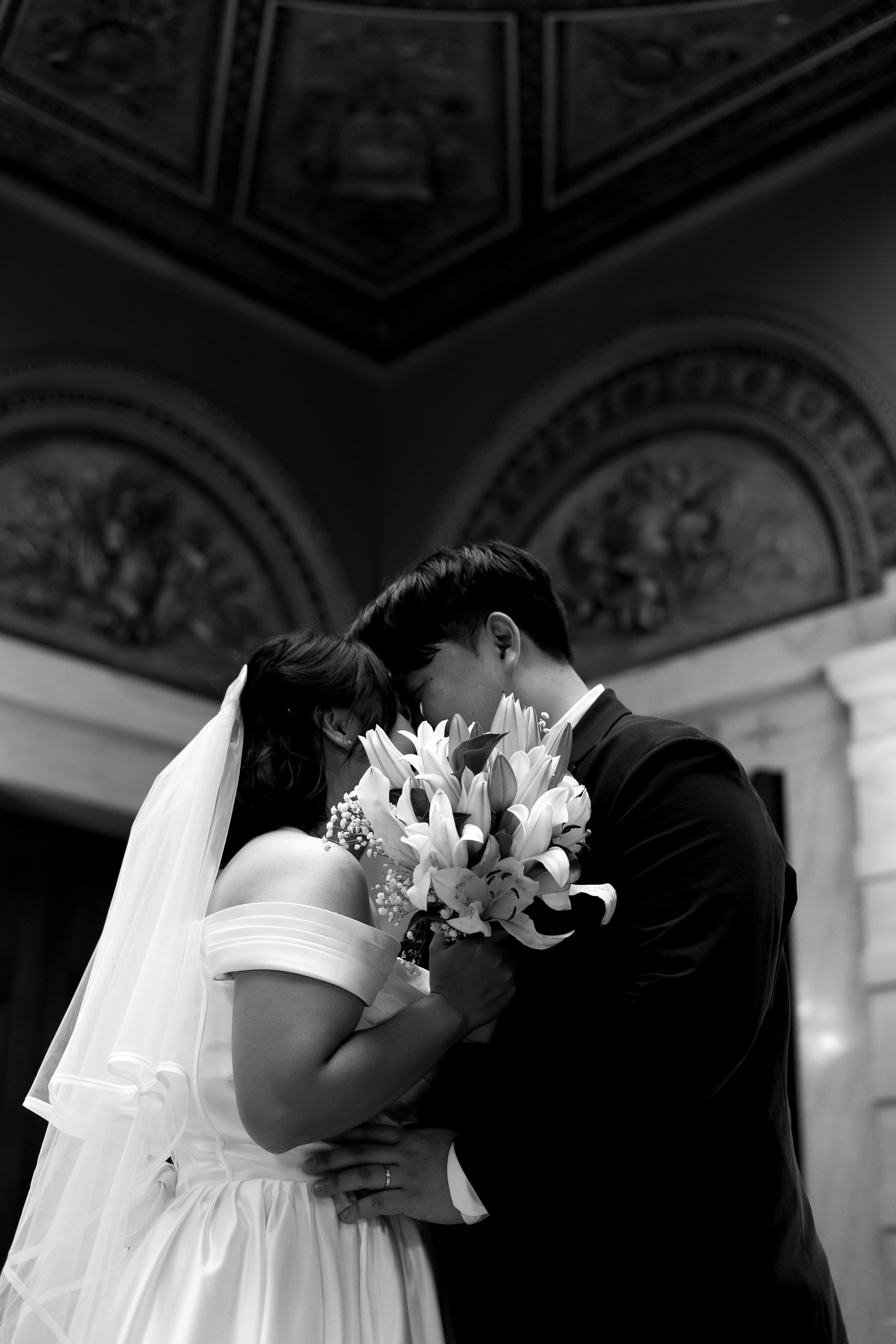 Couple kissing while holding a bouquet in front of their faces