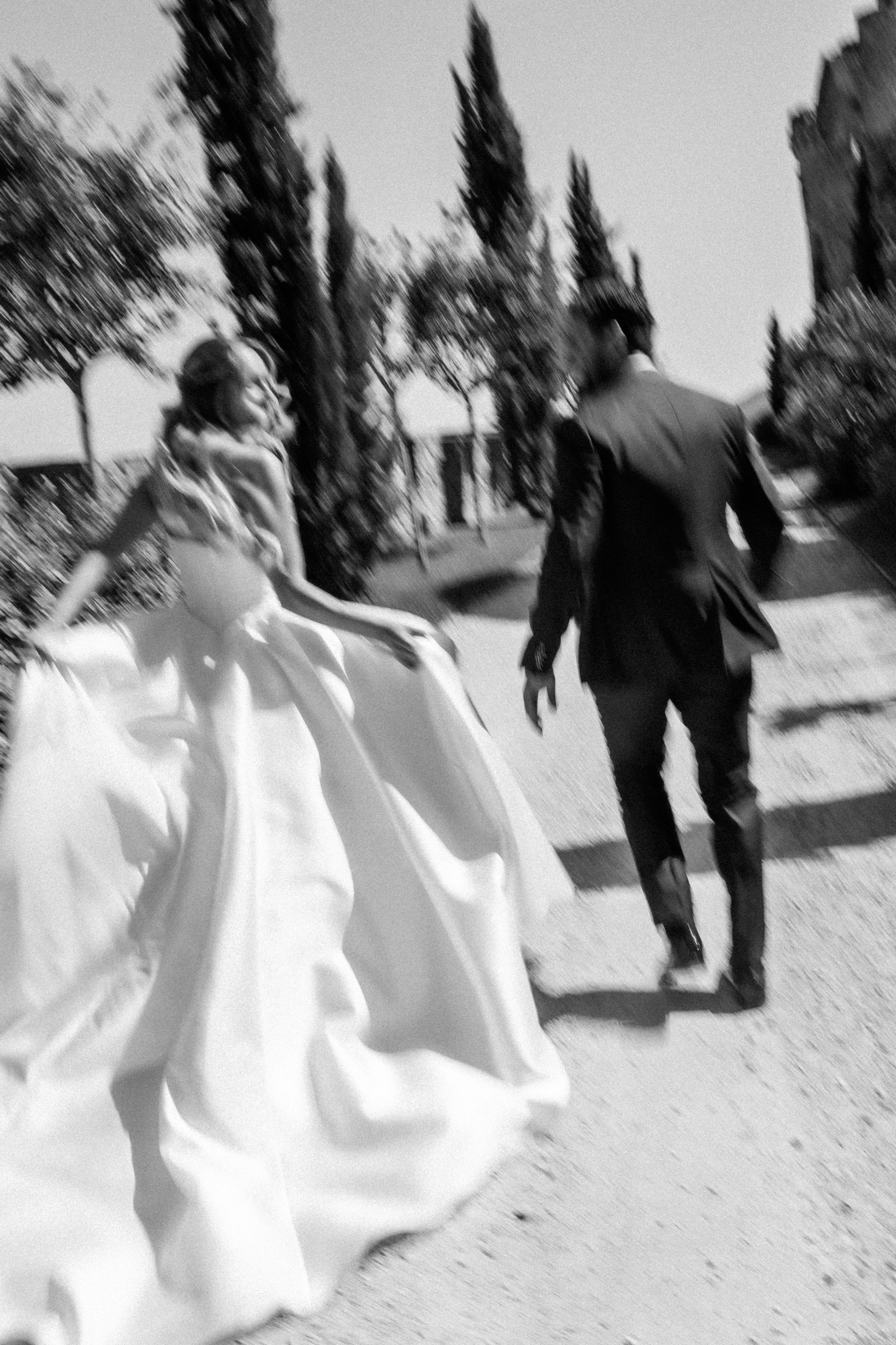 Black and white photo of the bride and groom running past the cypress trees