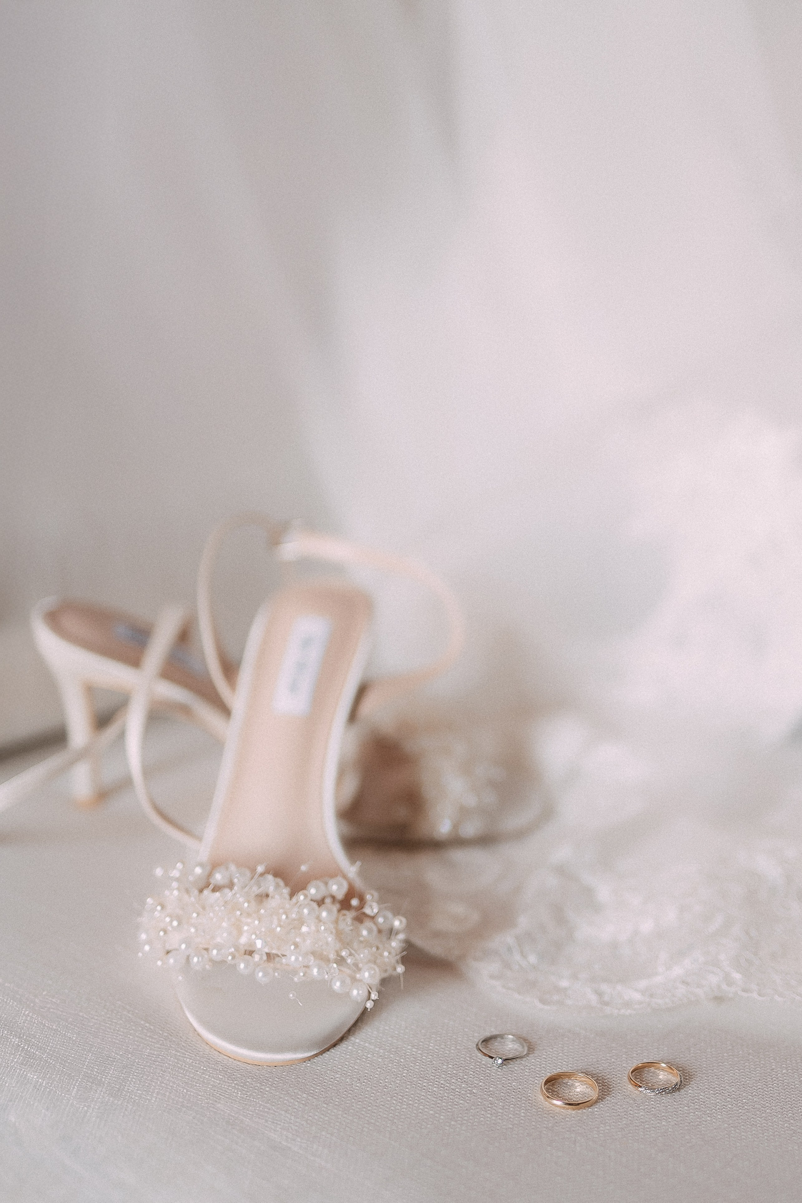 Bridal shoes with pearl detail and wedding rings resting on the veil