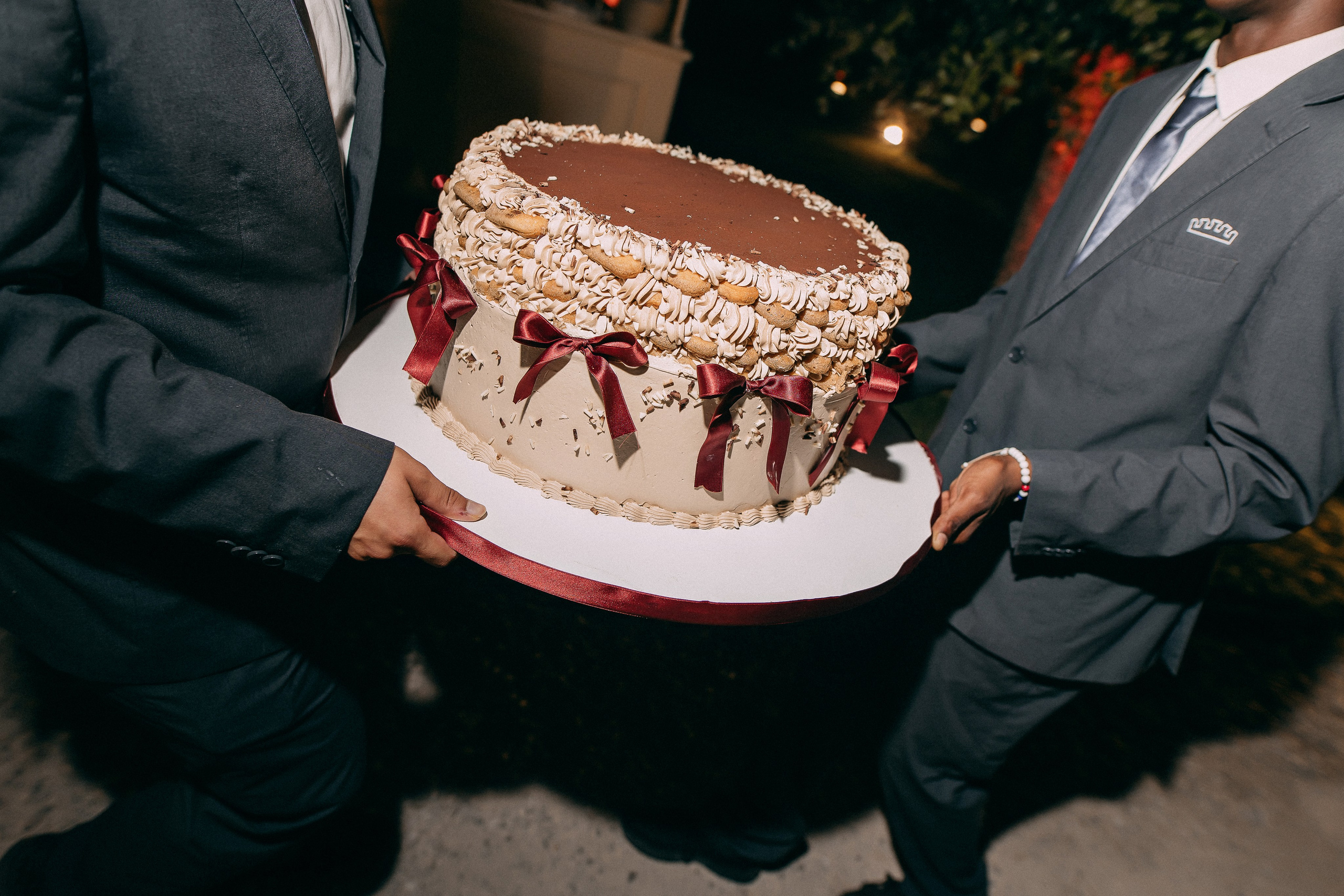 Groom carrying the wedding cake decorated with red ribbons