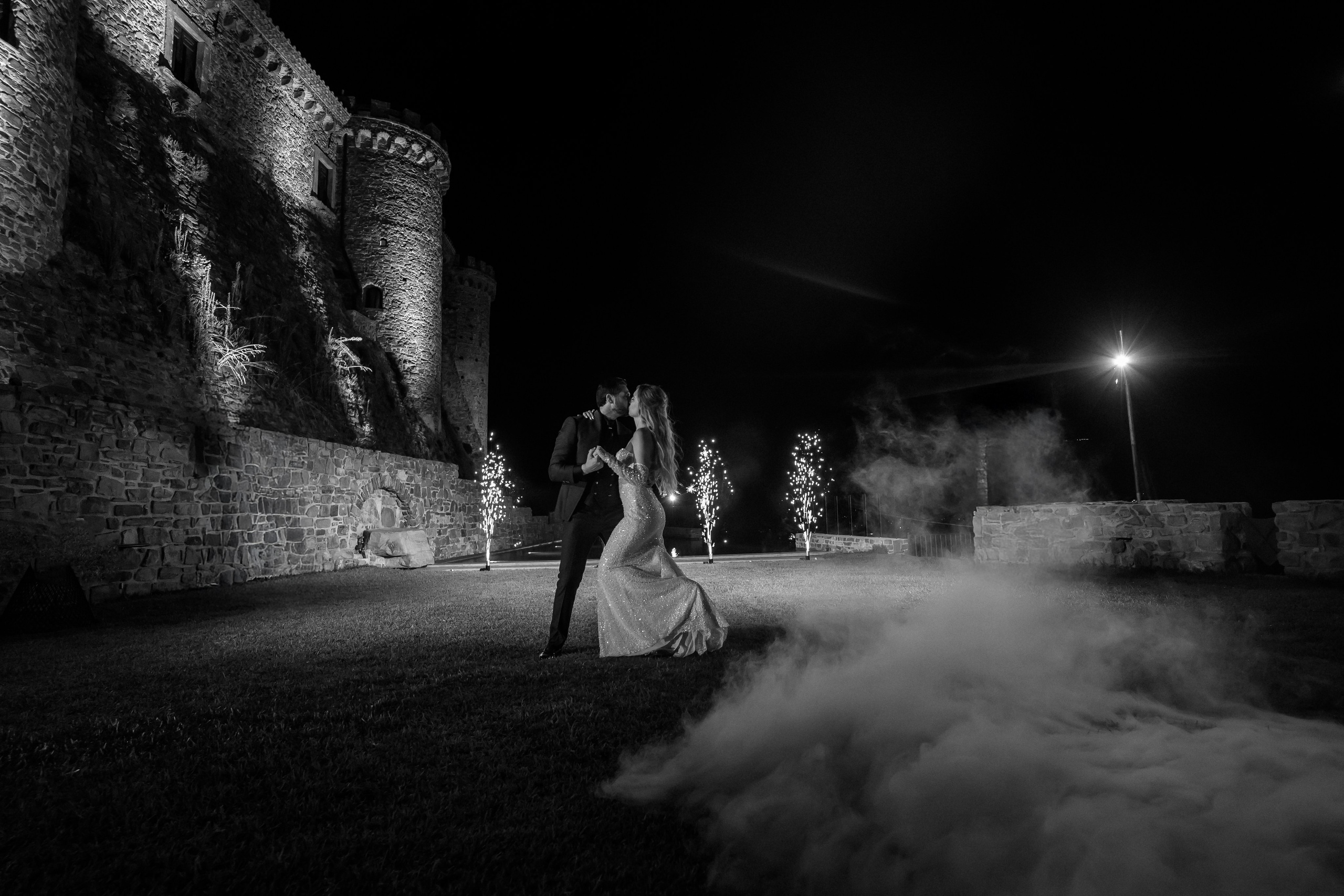 Bride and groom dancing in the fog beneath the lit castle walls