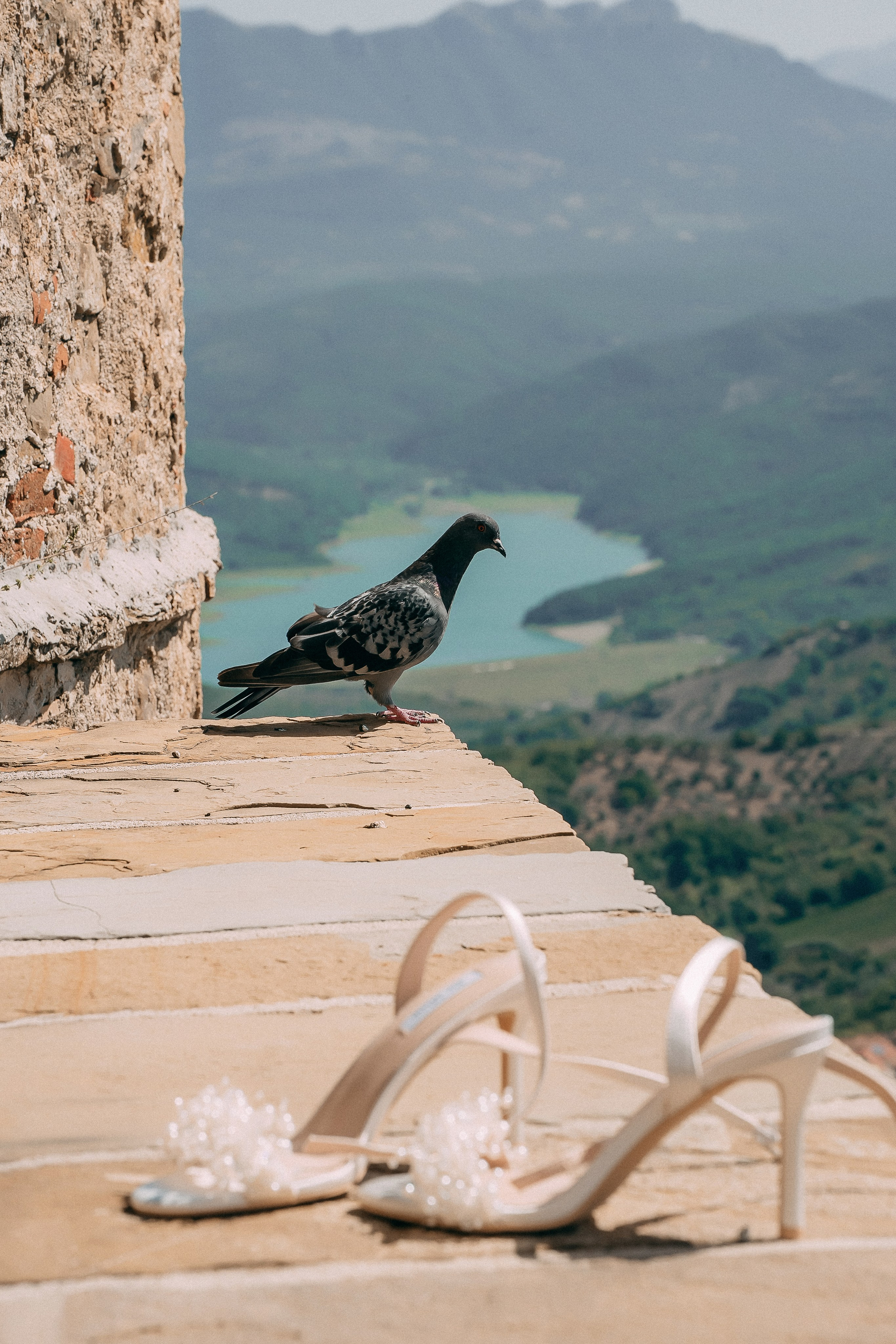 Pearl bridal heels on the castle wall with a pigeon and the Cilento valley behind
