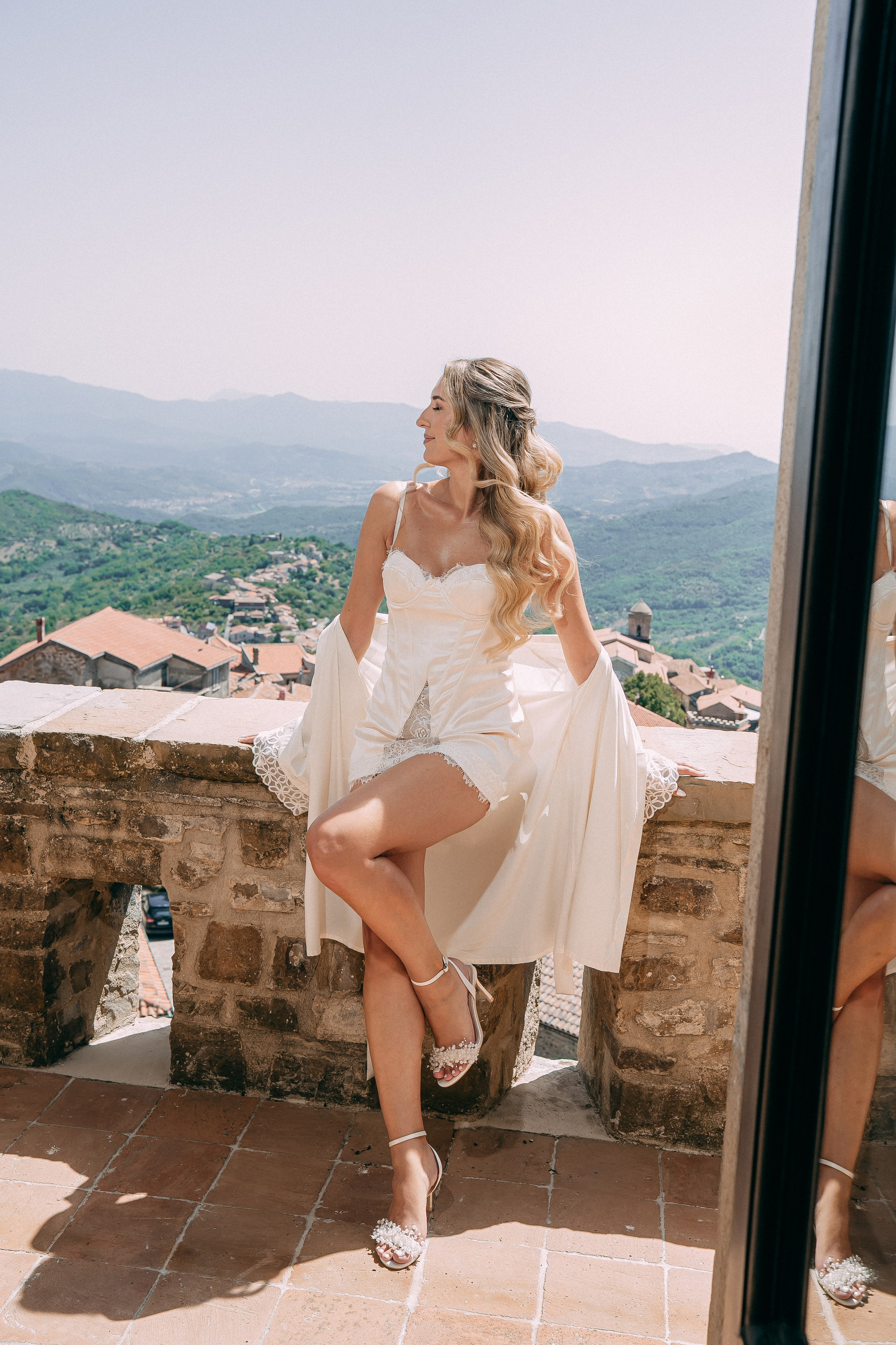 Bride relaxing on the castle wall with the village rooftops behind her