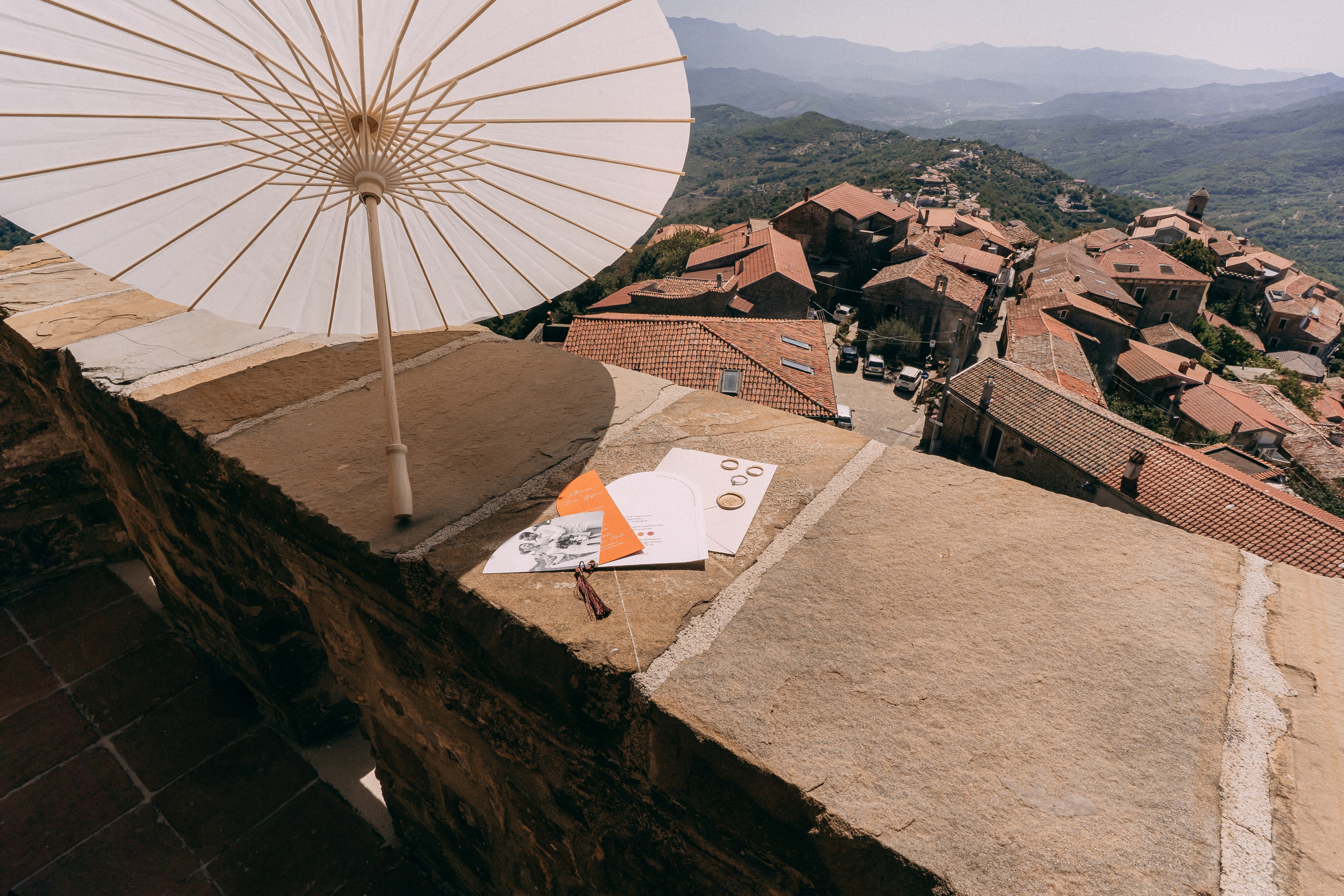 Paper parasol and wedding stationery on the castle wall overlooking the Italian countryside