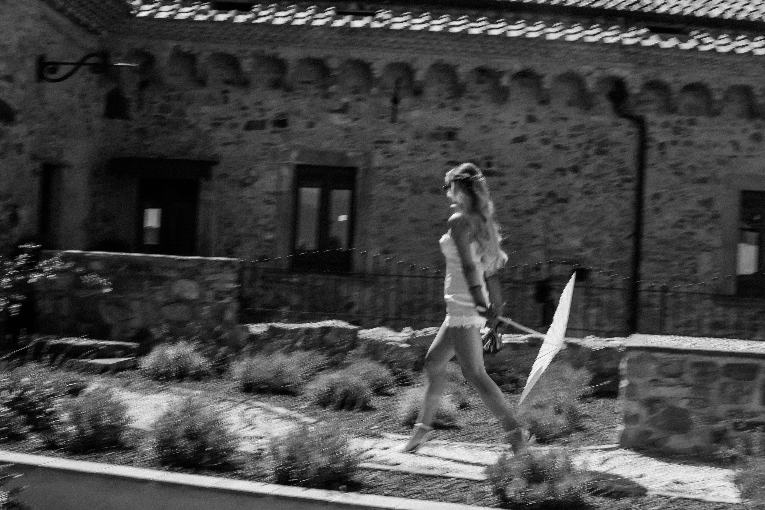 Bride walking with her parasol past the stone walls of the castle