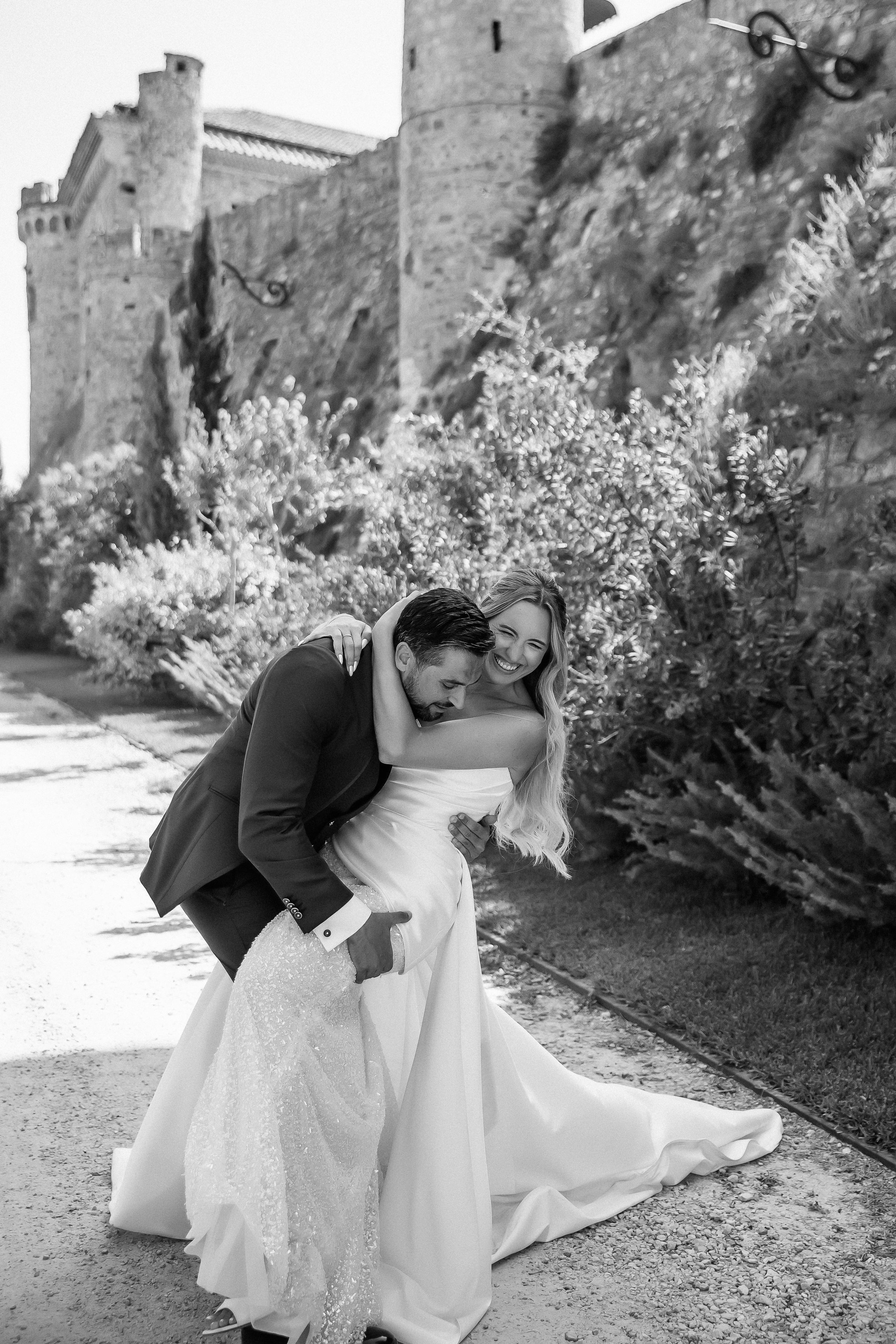 Black and white portrait of the newlyweds embracing by the castle wall