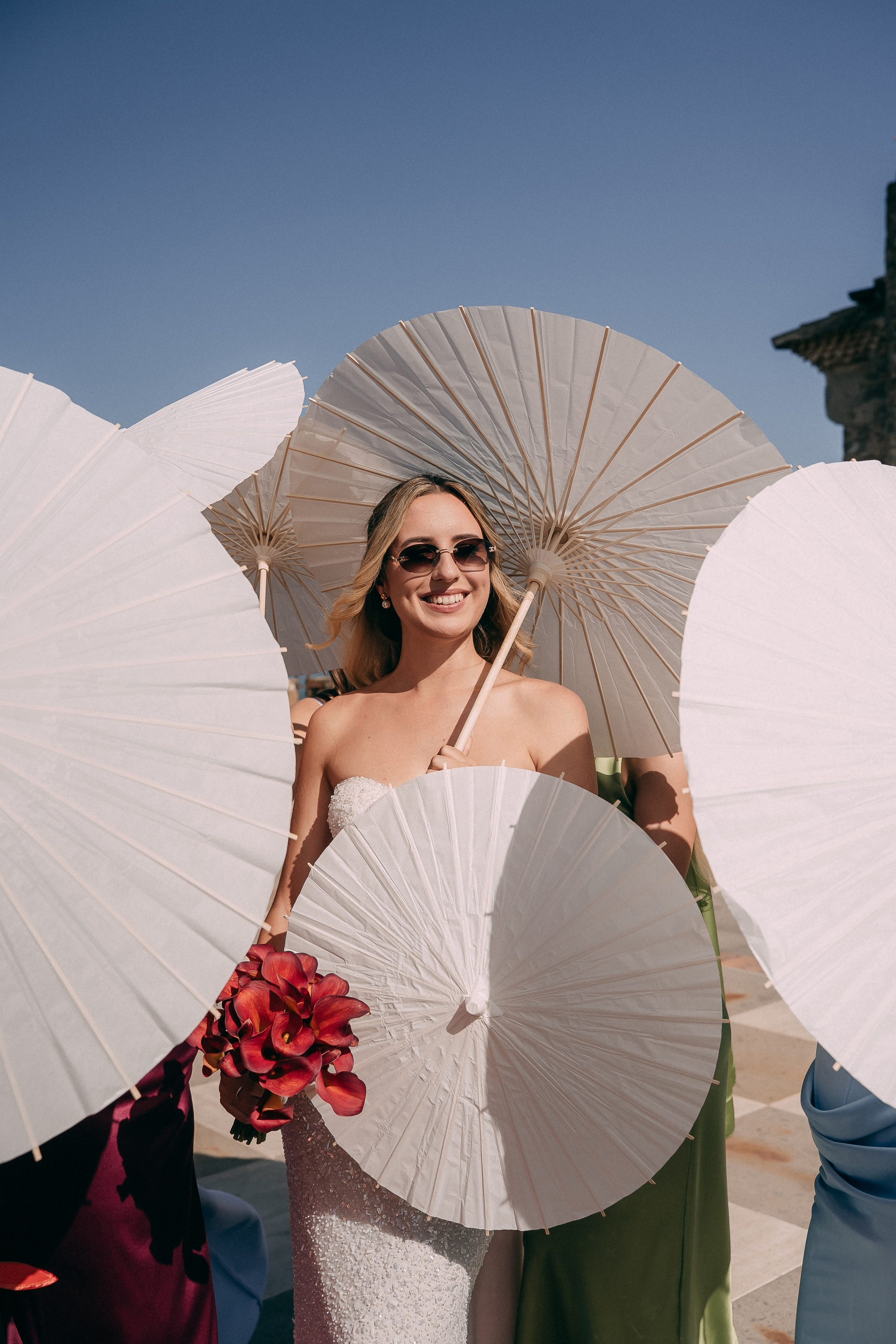 Bride with a red bouquet surrounded by parasols before the ceremony