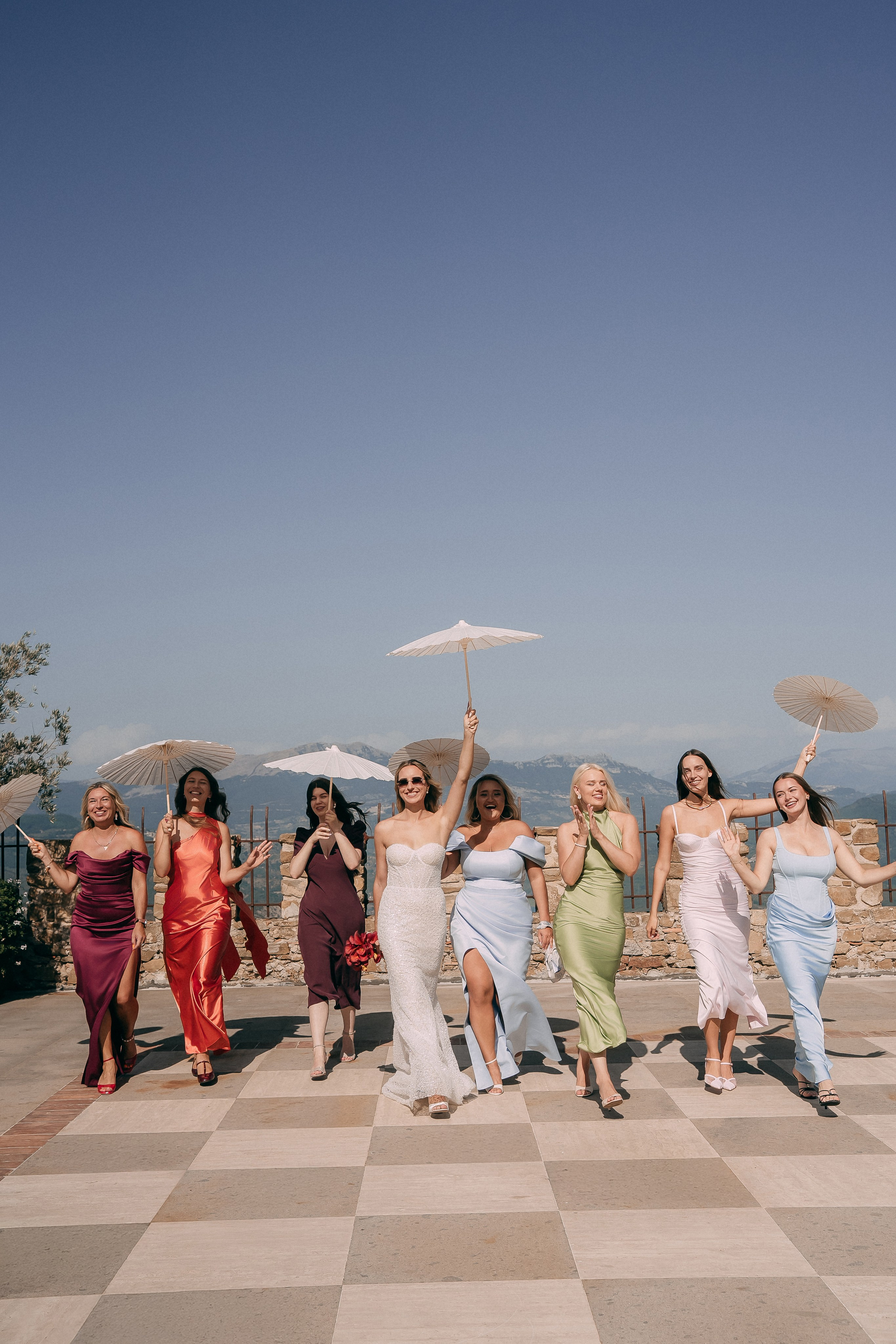 Bride and bridesmaids walking with paper parasols on the checkered terrace