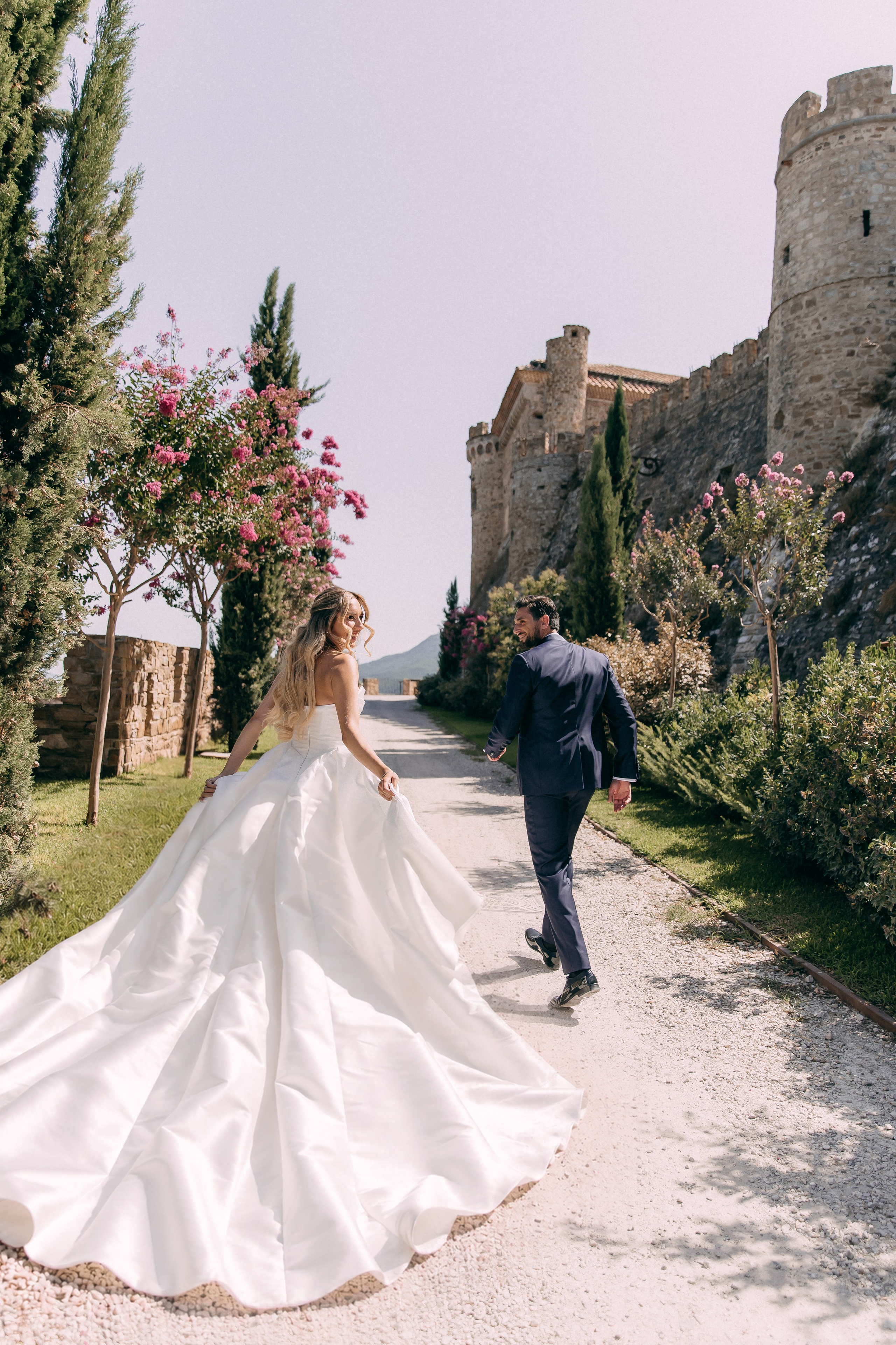 Bride's long train sweeping the path with the castle walls behind