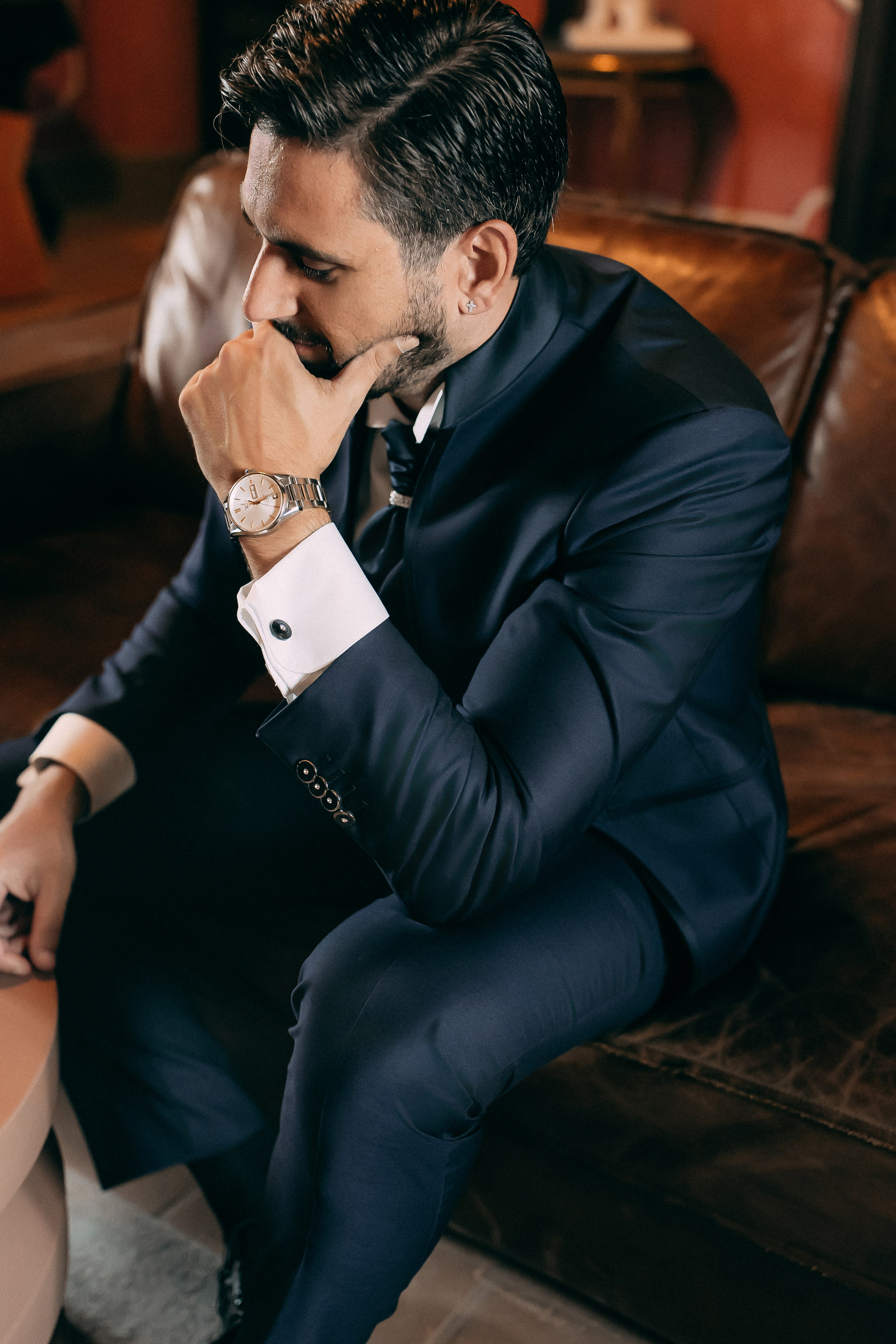 Groom adjusting his cufflinks in a leather armchair before the wedding