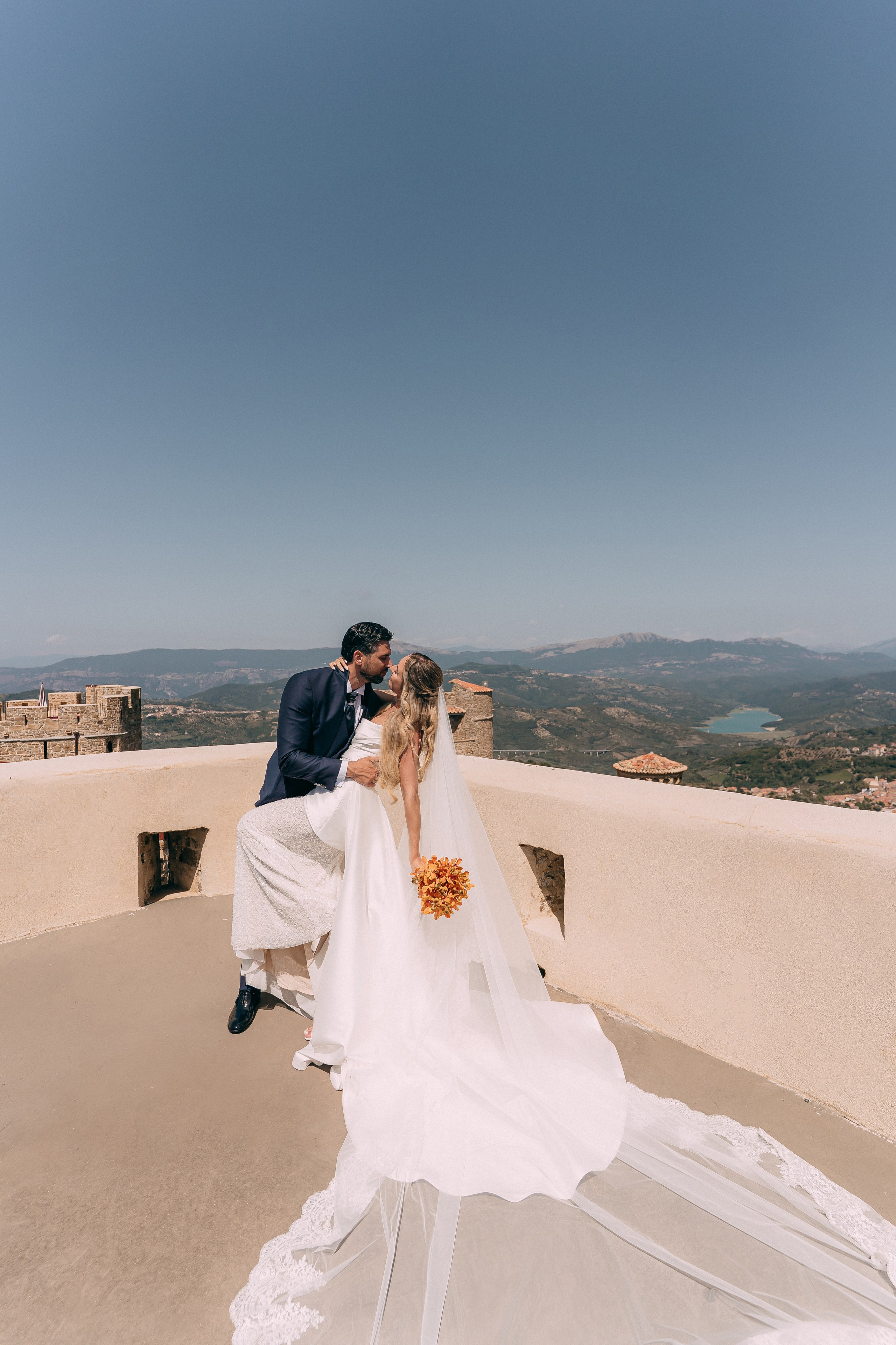 Groom kissing the bride on the castle rooftop above the mountains