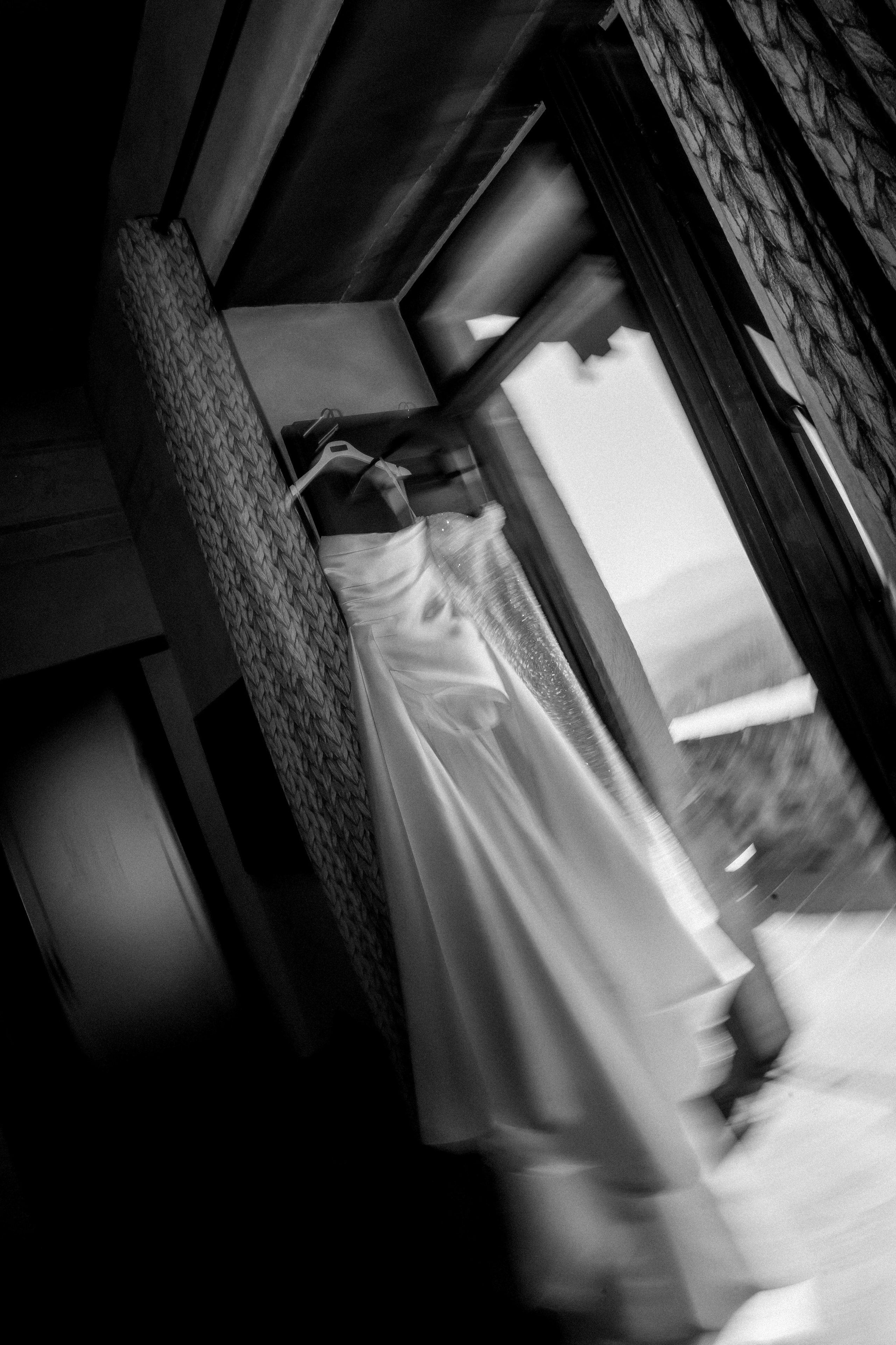 Black and white photo of the wedding dress hanging by a window in the bridal suite