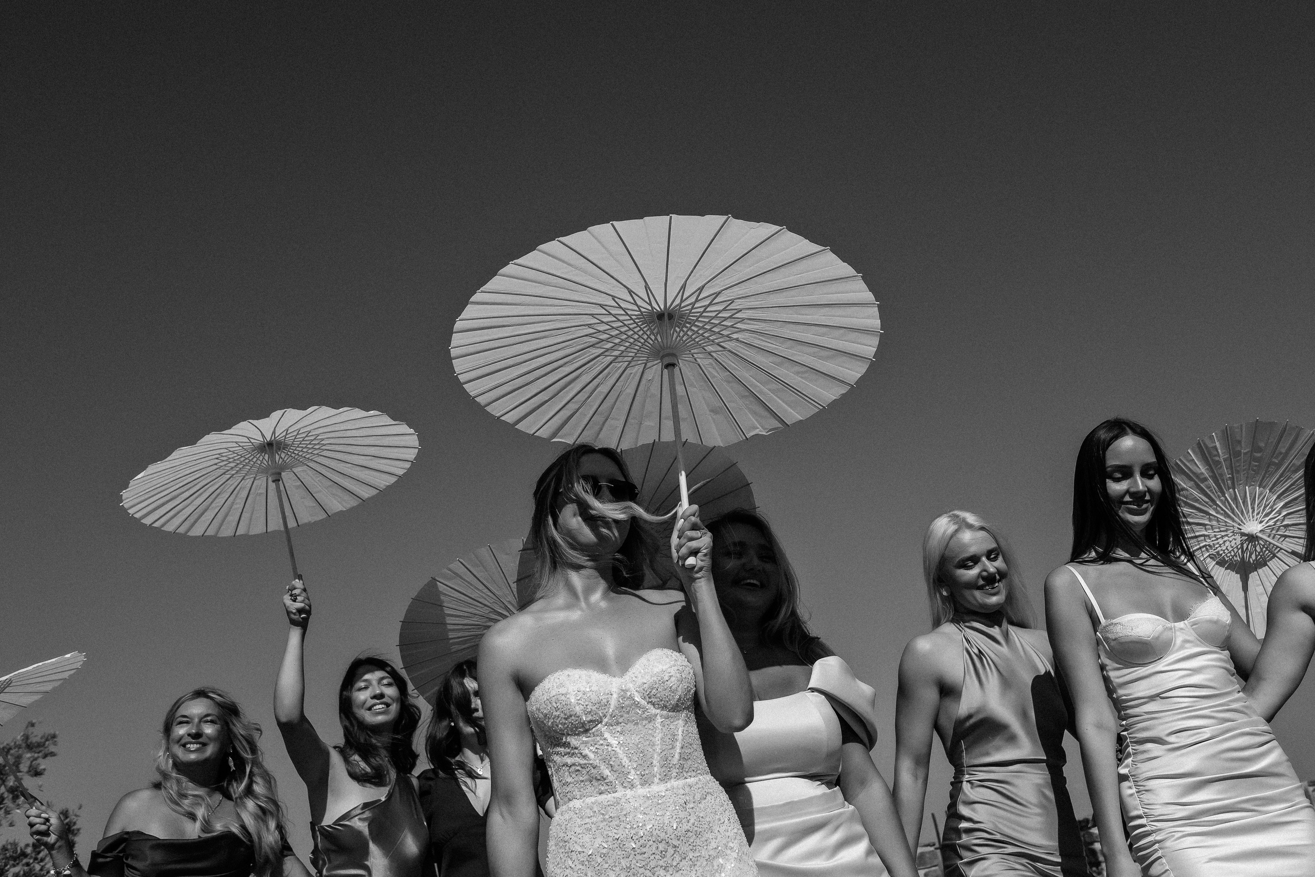 Bride and bridesmaids celebrating with parasols against the sky