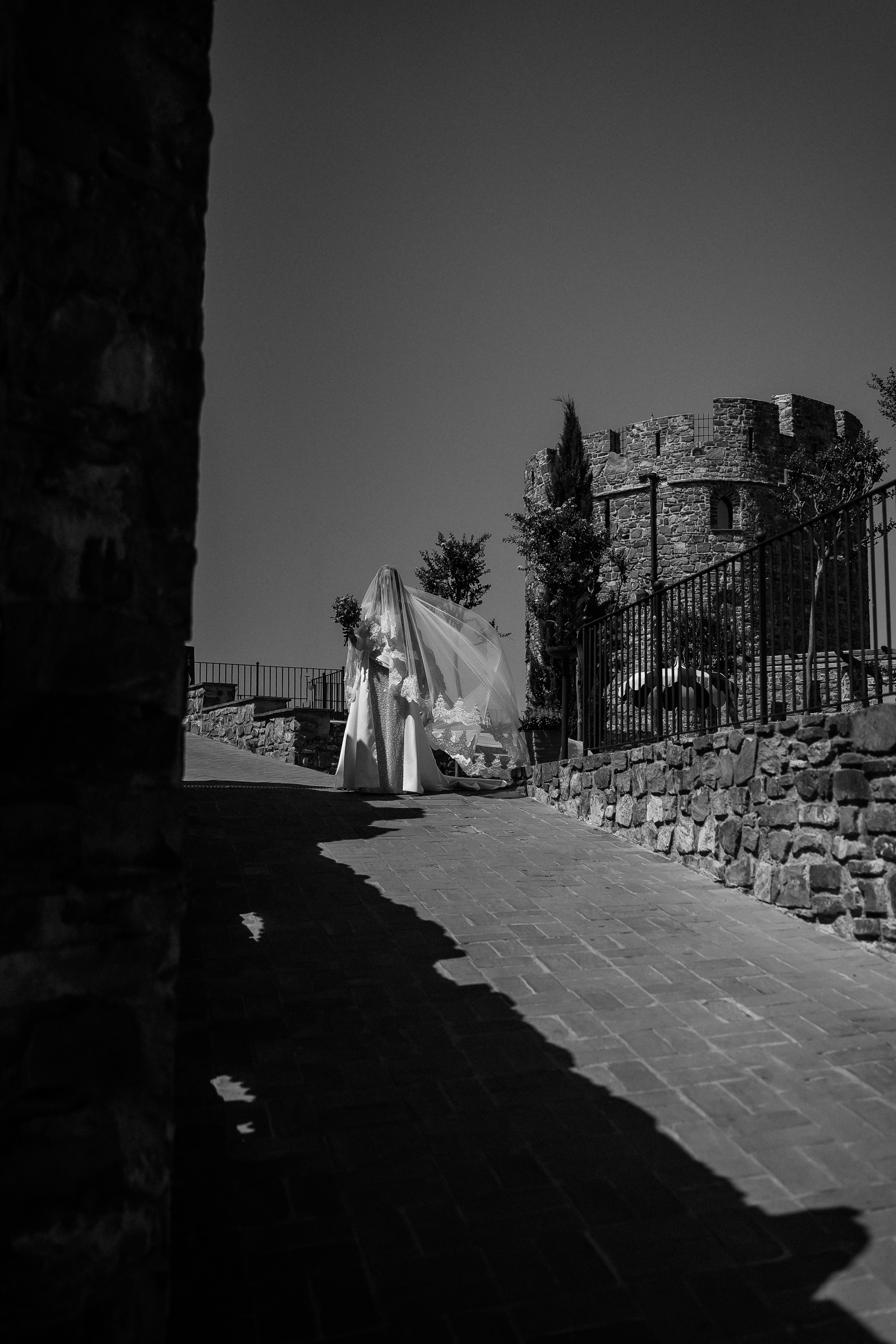 Black and white photo of the bride's veil catching the wind by the castle gate