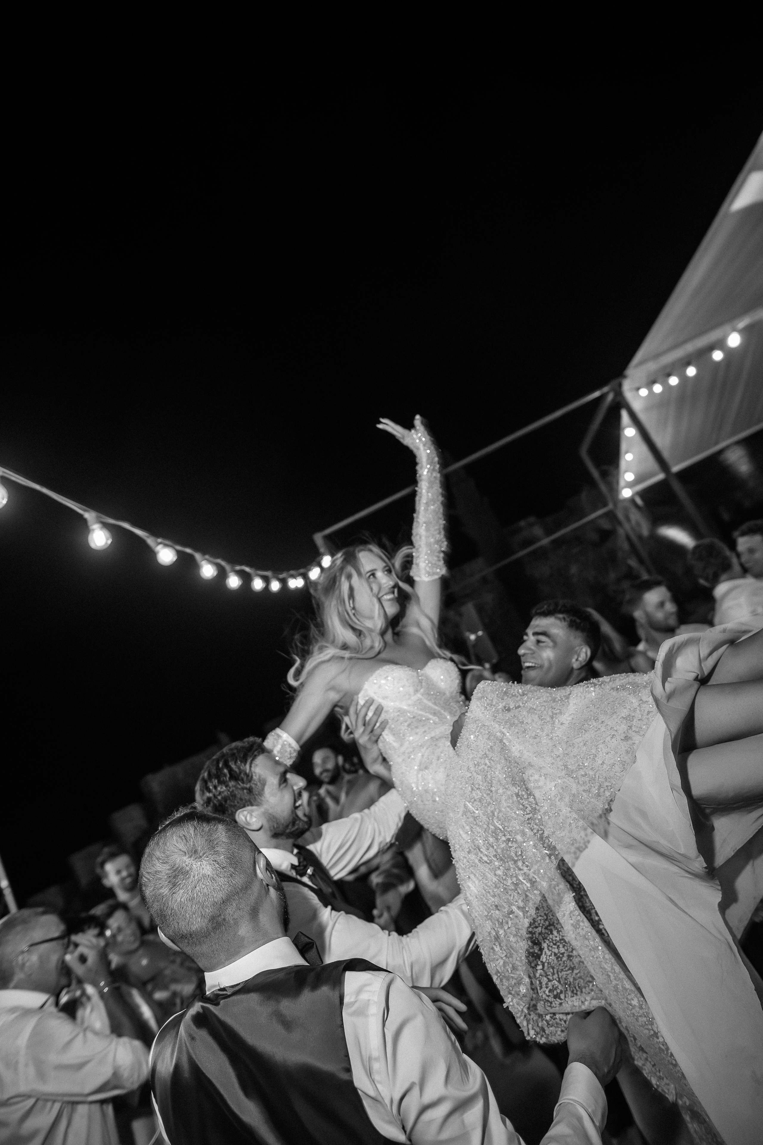 Black and white photo of the bride being lifted by dancing guests