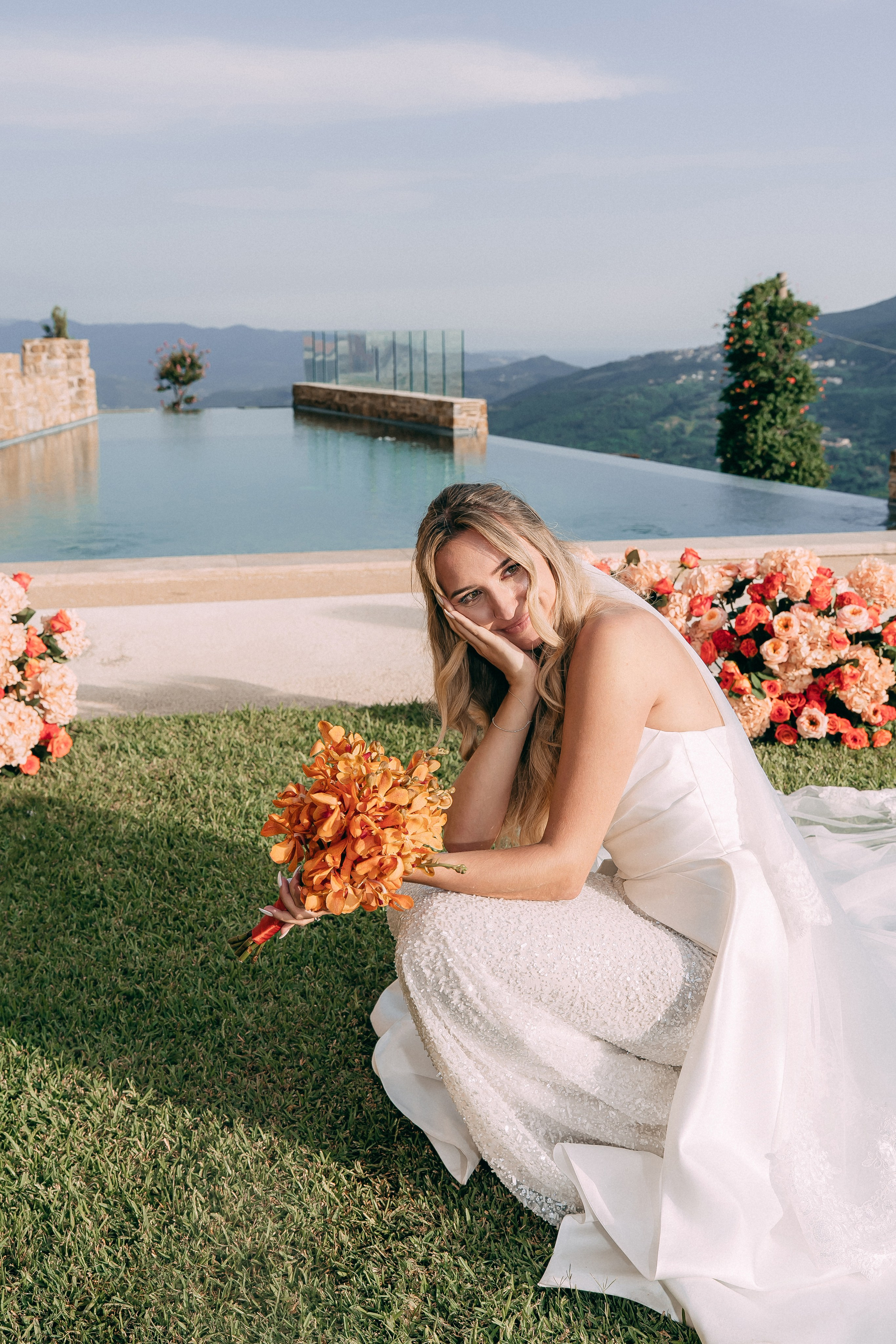 Bride with her orange bouquet sitting by the infinity pool